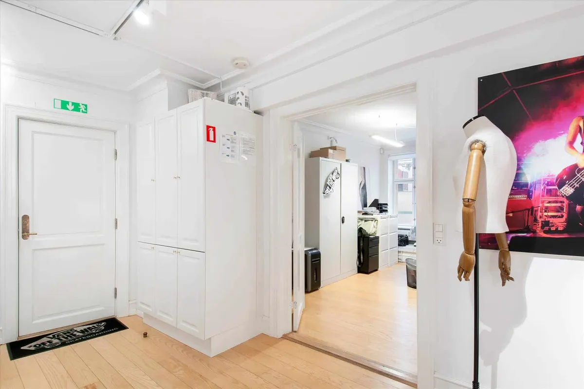 Køkken med vandkøleskab, trægulv og åbent kammer, ligesom der er en manuel ståstol og et foto af en musiker på væggen