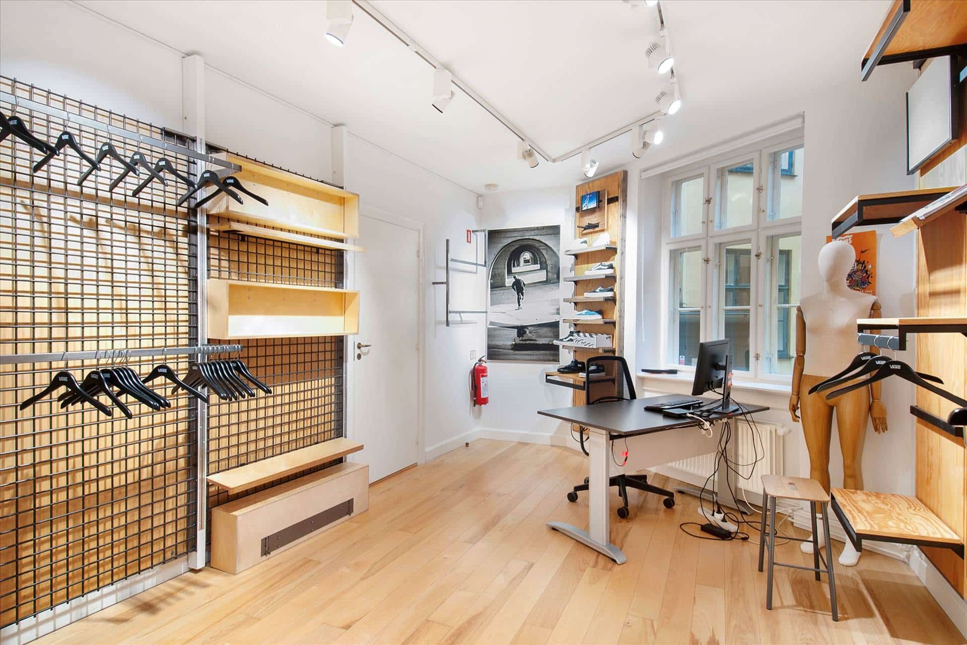 En kontorplads med tre stole, et bord, og to dukker i en ramme med hængehylder og sko på hylderne