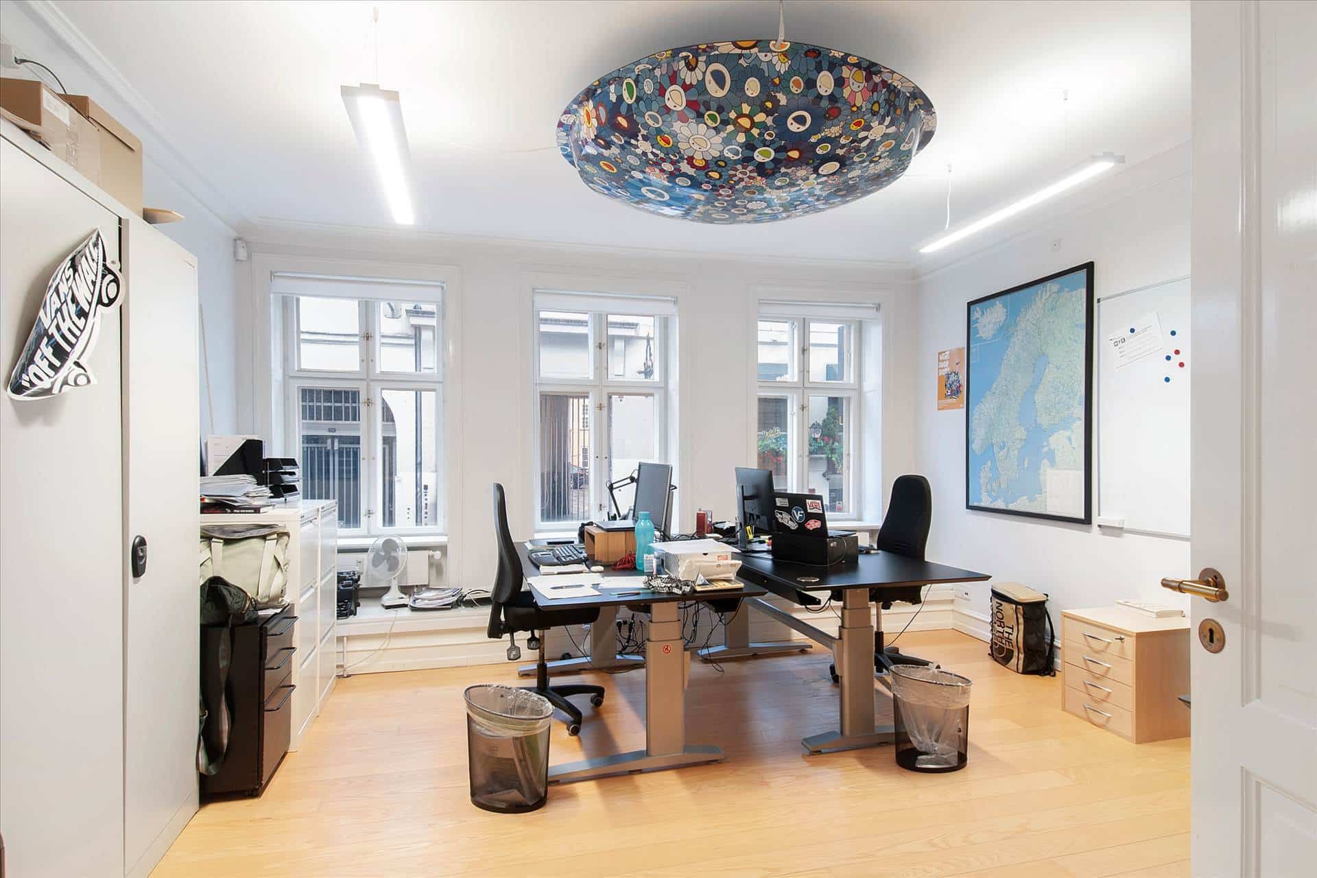 Kontor med to skriveborde, høj kvalitetsmøbler og en stor malet loftslampe i centrum af rummet