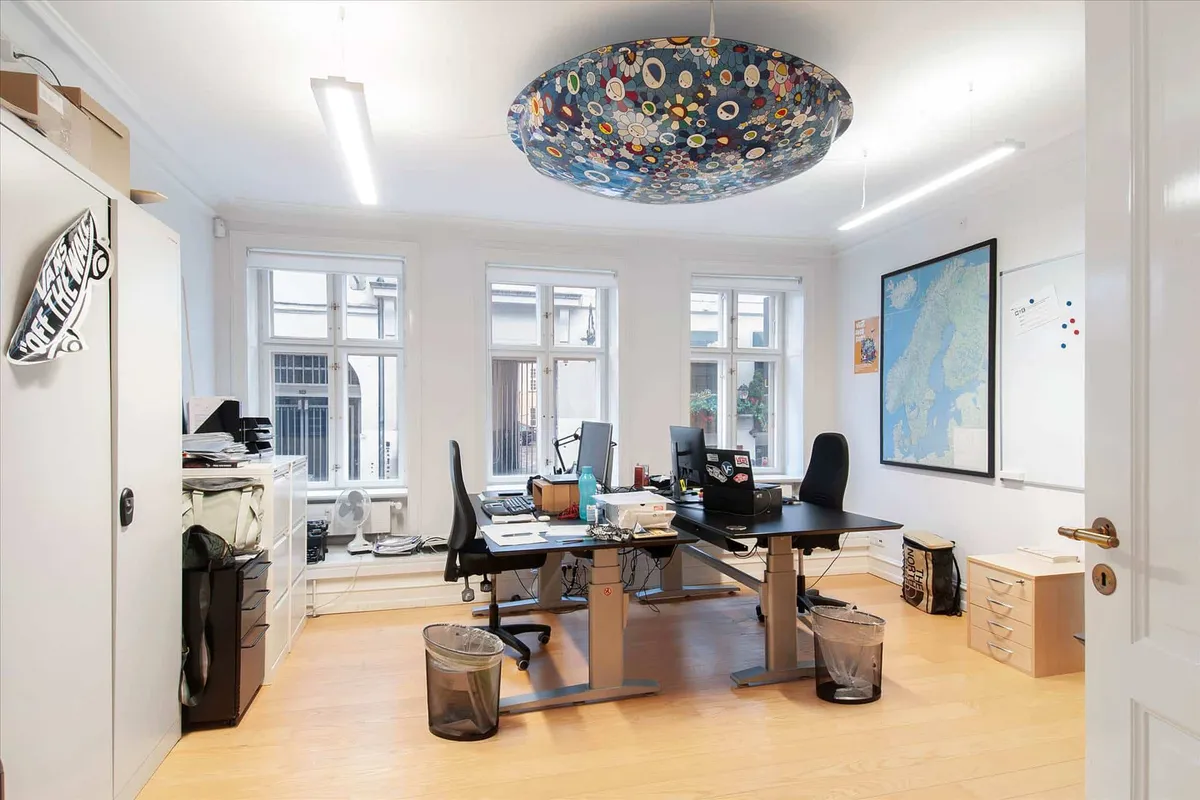 Kontor med to skriveborde, høj kvalitetsmøbler og en stor malet loftslampe i centrum af rummet