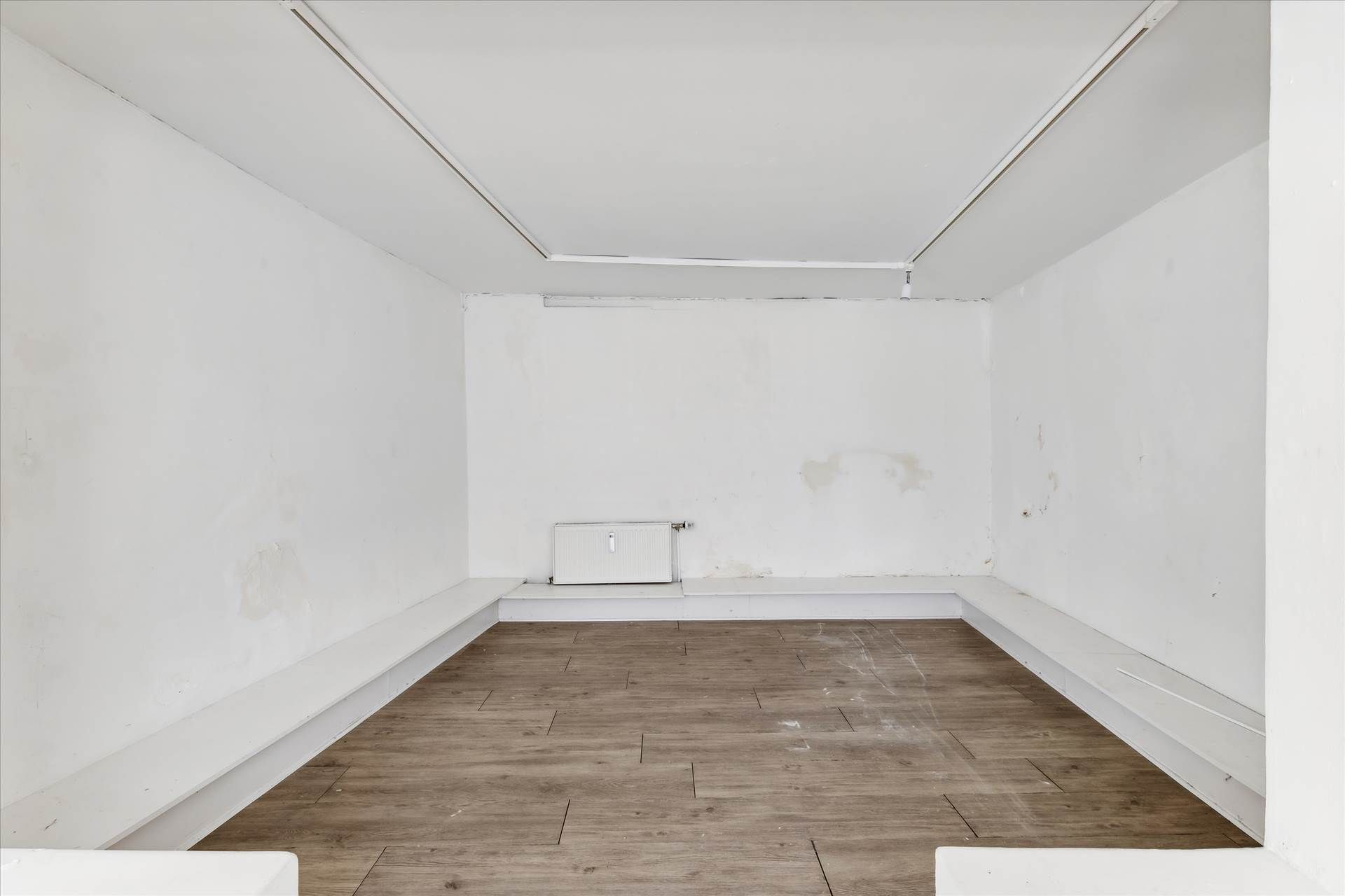 En hvidrum med lysegul gulvbelægning og hvide vægge samt hvide skrå senge langs væggene og en radiator i bagvæggen