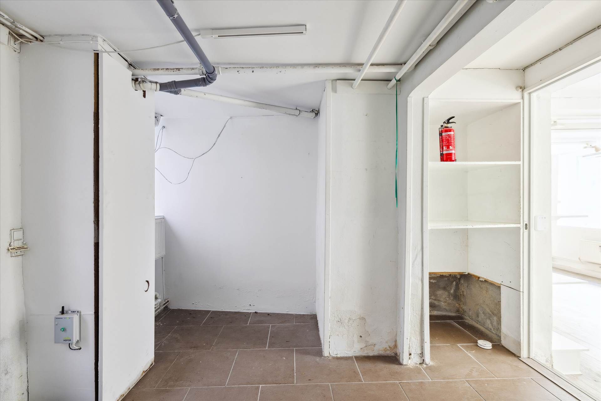 Kort gang med åbne døre og en hvid kasse, hvor der er en brandhætte placeret på en høj hylde