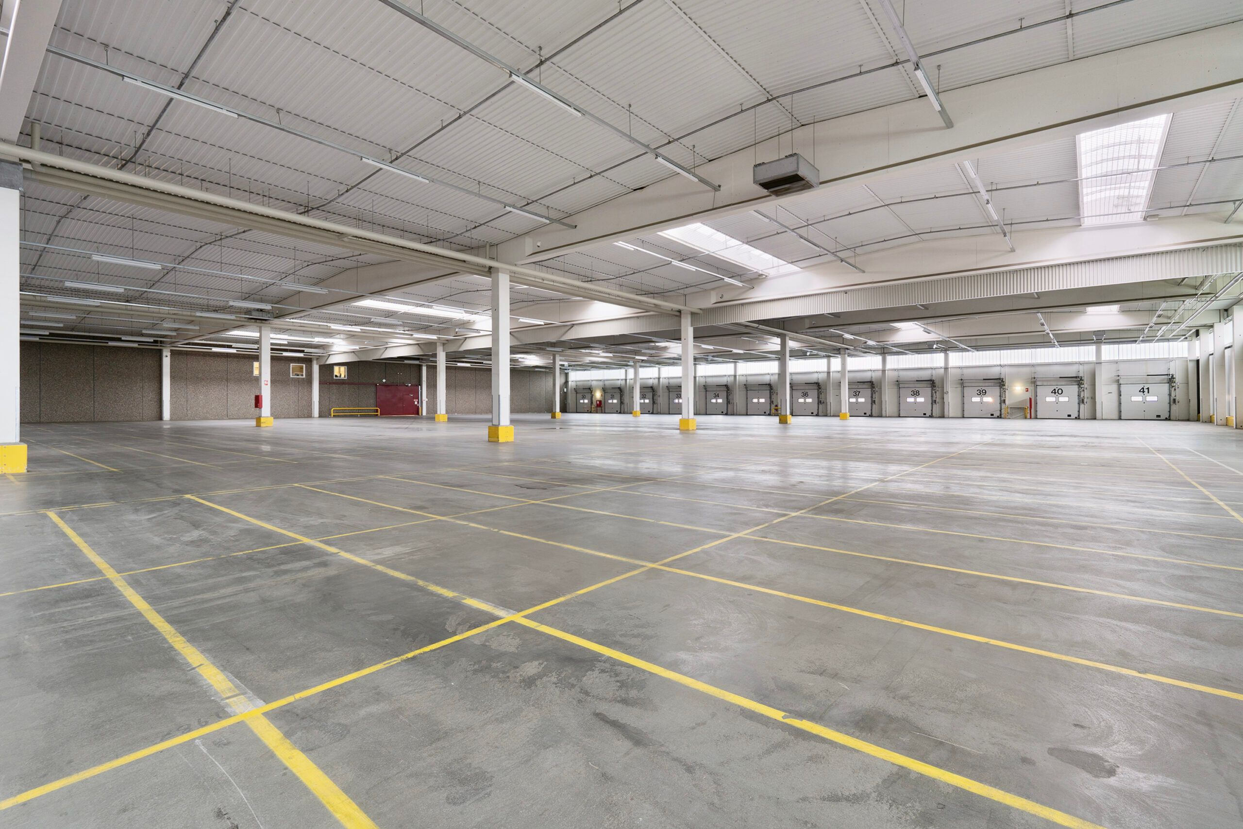 Lagerbygning med gult og hvidt malet gulv og gulve og hvide søjler og højt til loftet med hvide lofter og lyse skygger fra