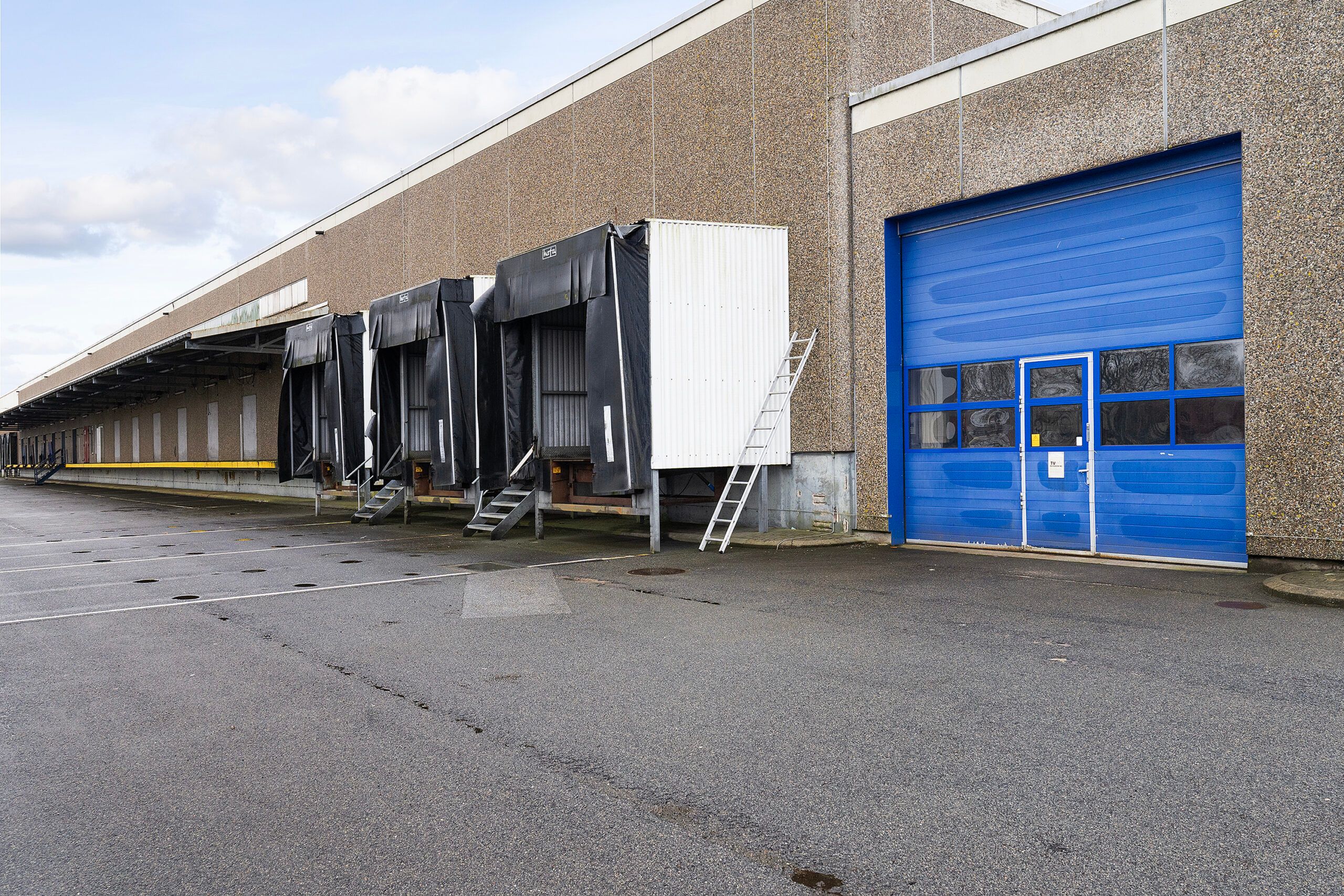 Lagerbygning med hvide og sorte rulledøre, hvor hvert dørsæt har en trappe og en stige til siden.