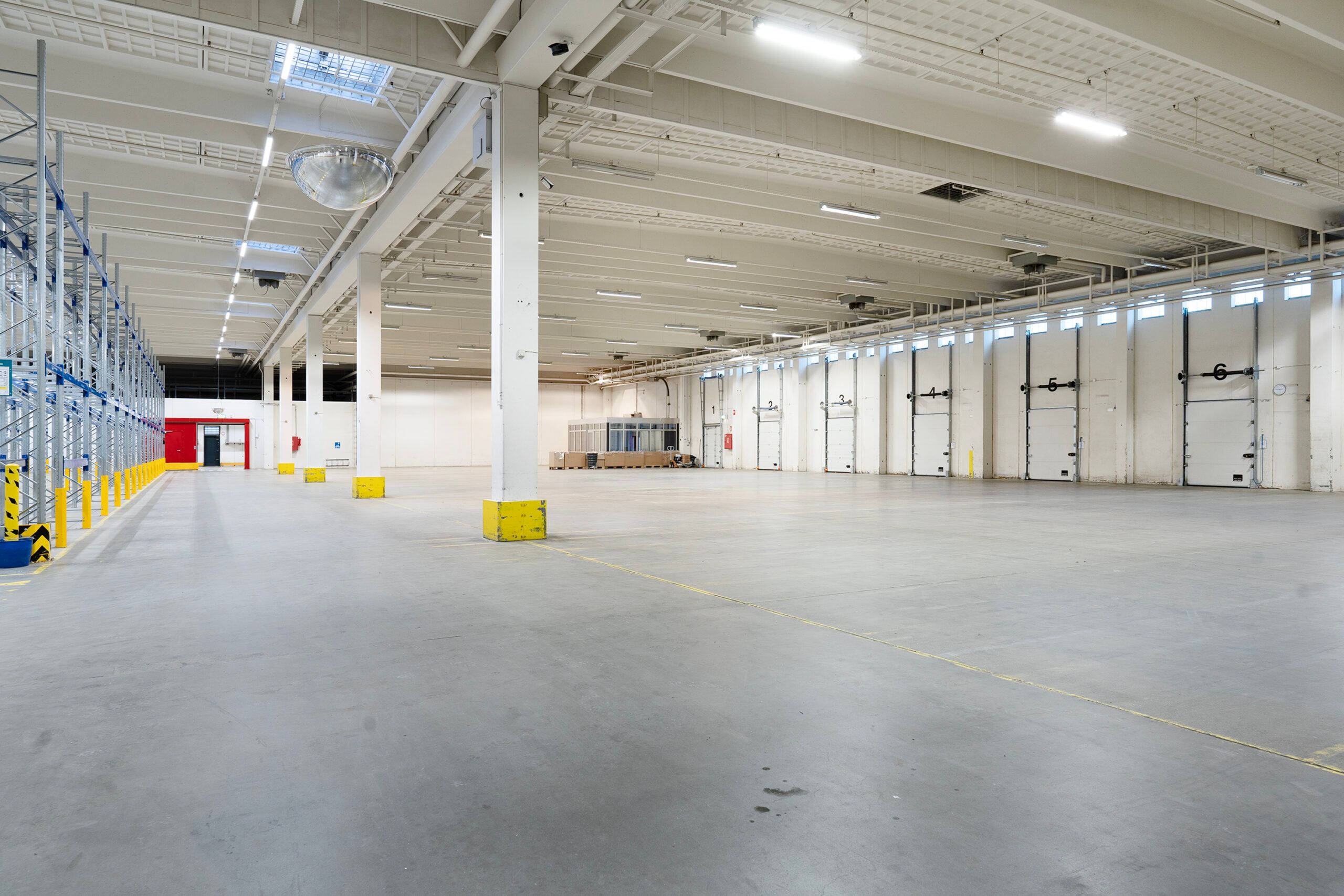 Lagerhal med store, hvide døre, gul gulvmærkning og metalbåresystemer langs væggen.