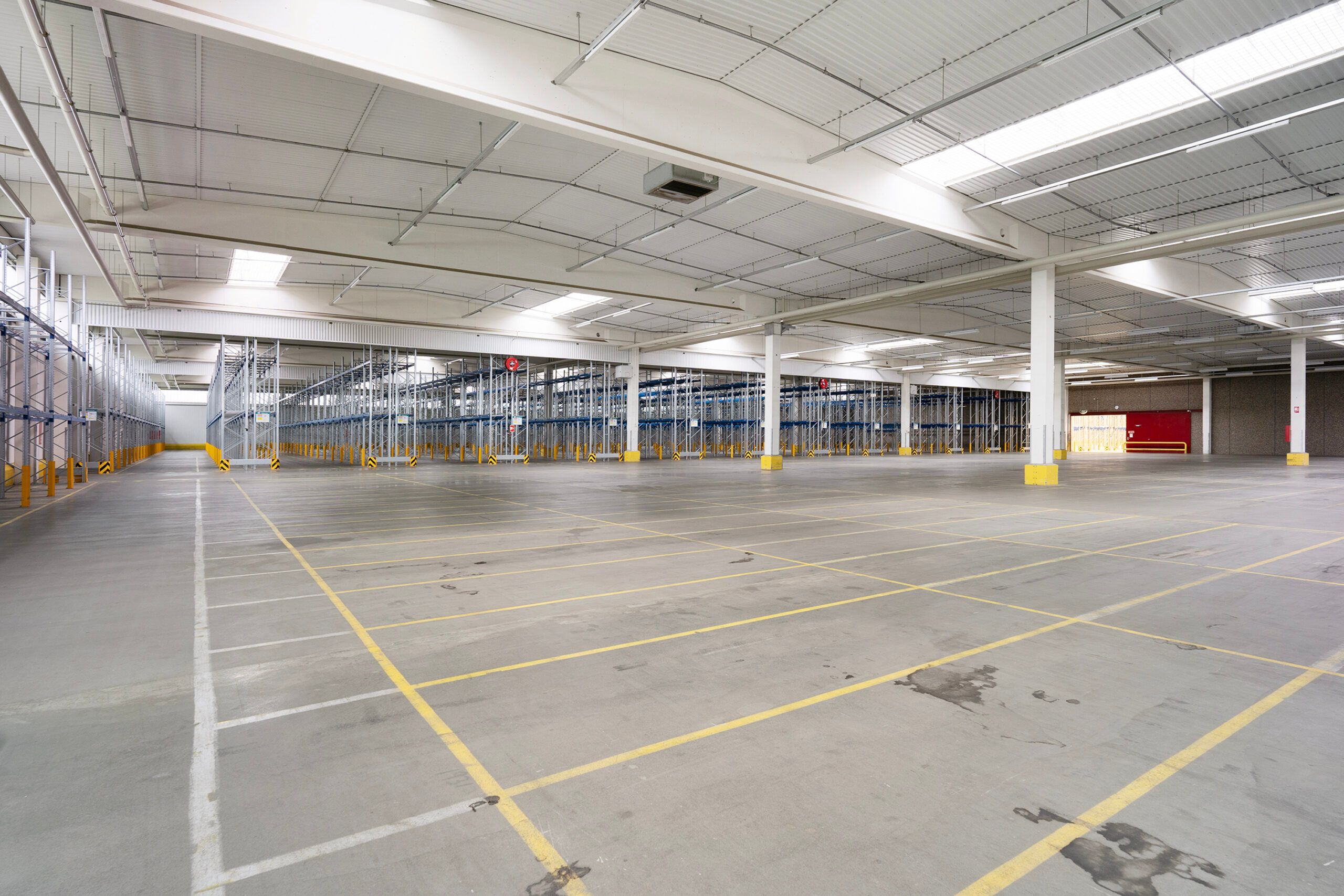 Stort lager med gul gulvmarkering og metalliske reoler i et tomt rum med lys på loftet