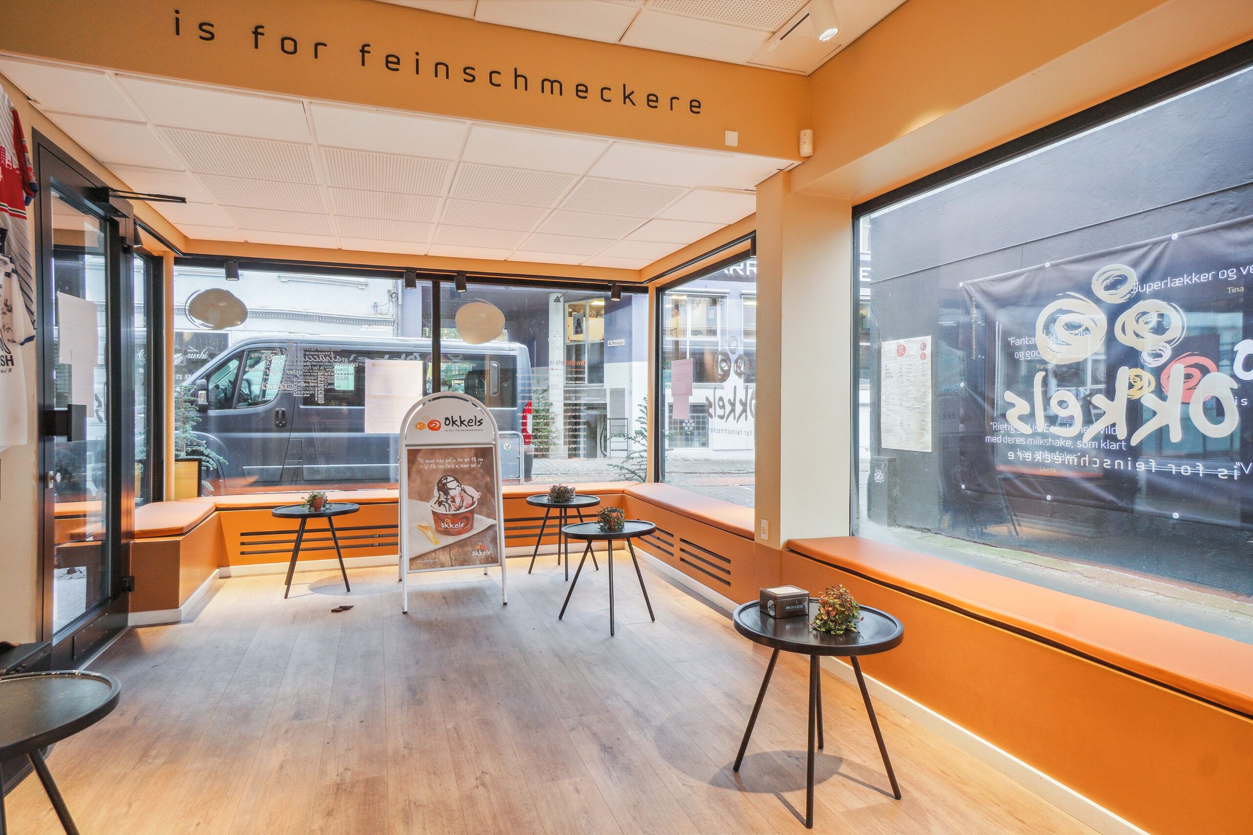 En moderne og møbleret lejlighed med store vinduer og orange accenter. Køkkenområde med lysegul væg og møbler i sort og