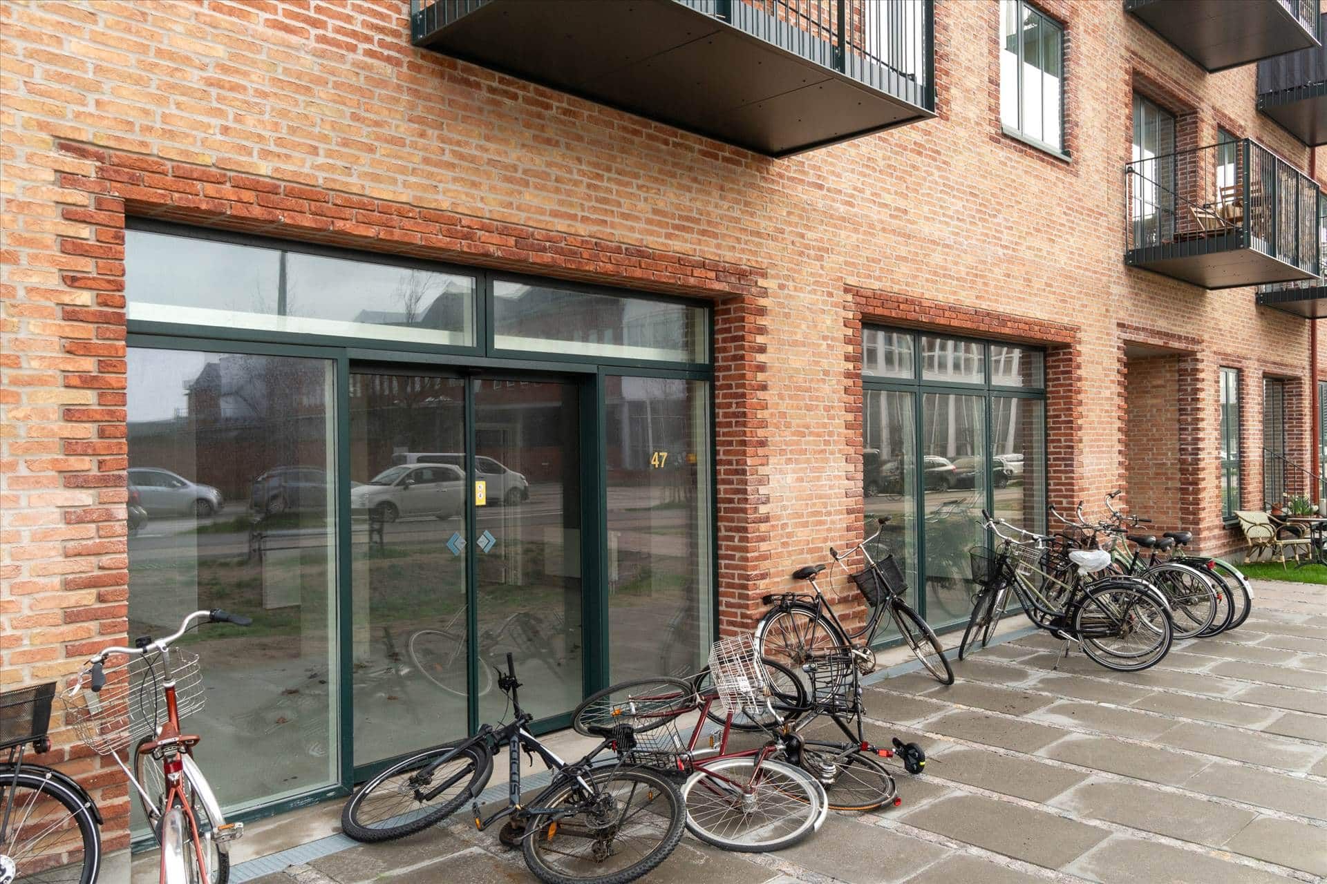 Flere cykler parkeret foran en bygning med glasruder og balkoner, adressen 47 står i et vindue