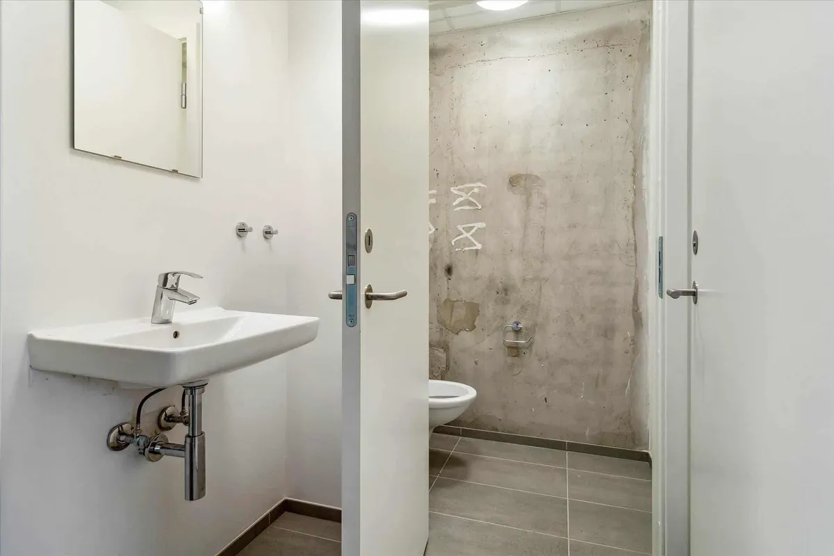 En hjørneplaceret renseri med et hvidt vasketøjsbælte og en hvid toilet med en høj toiletbrønd samt et skravebord med spejl