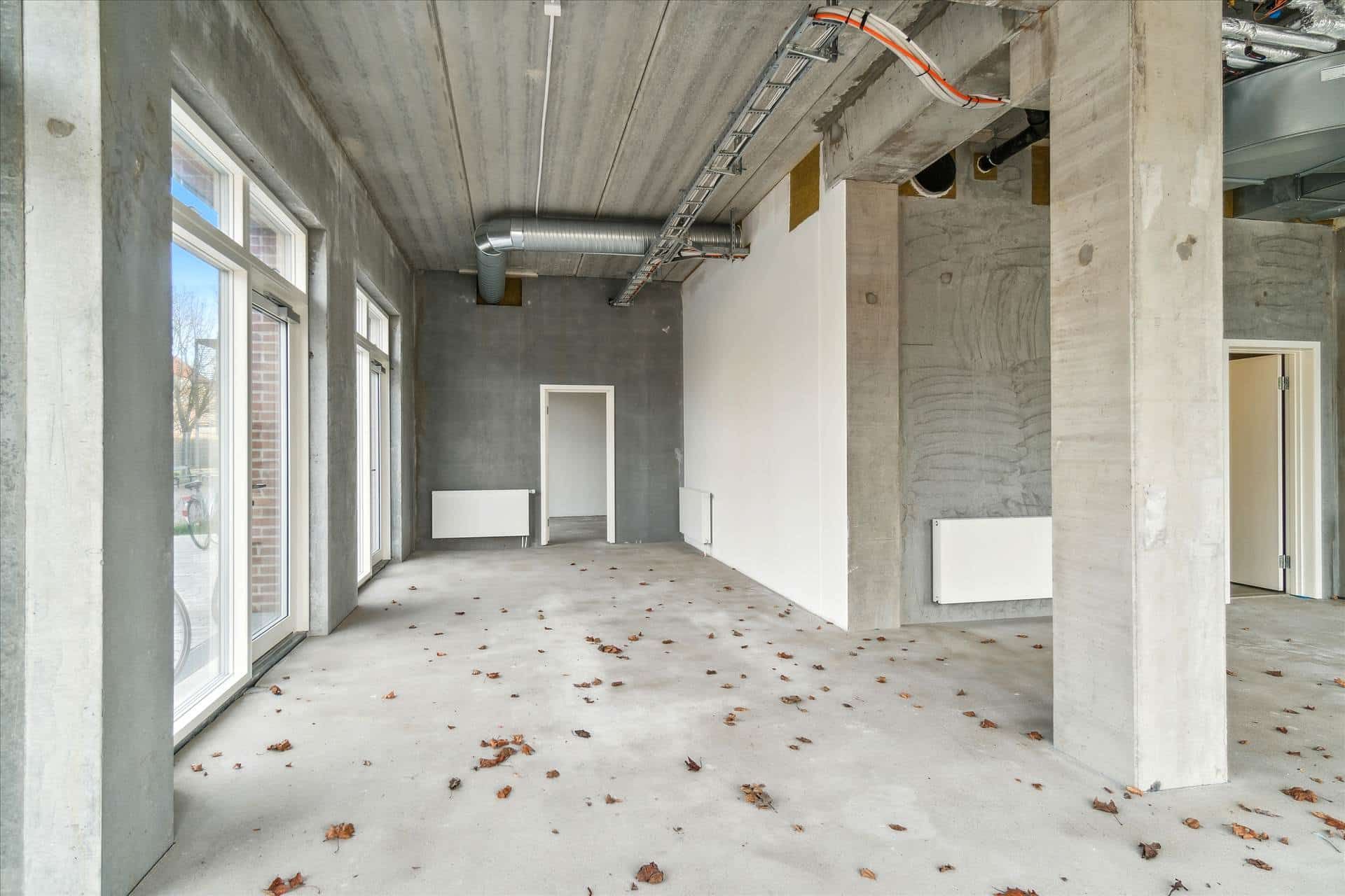 En tom erhvervslokal med cementgulve, høje hvide vægge og store vinduer med hjørnebeliggenhed og mulighed for udsugning