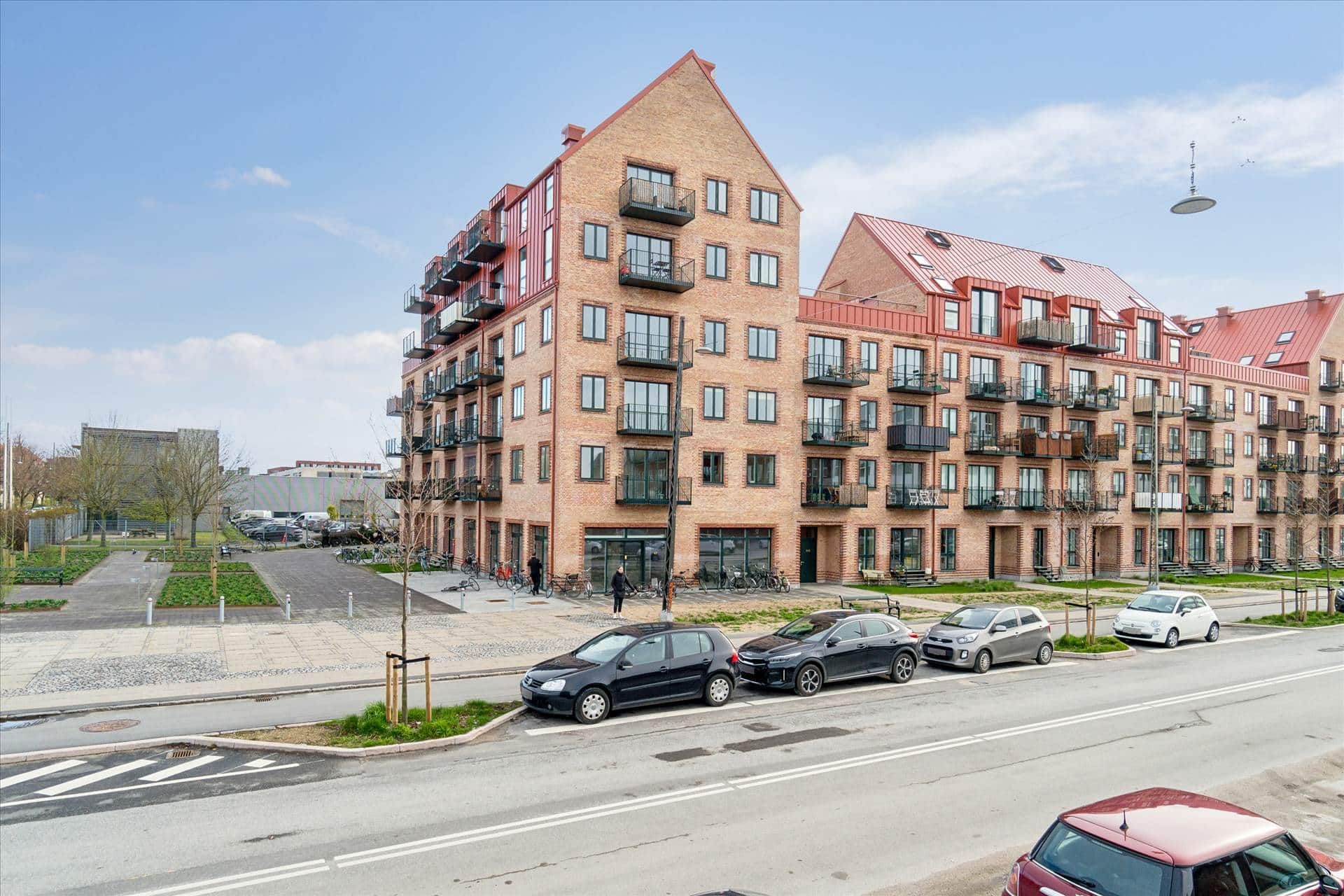 Tre biler parkeret ved siden af et rødt hus med flere terrasser og vinduer