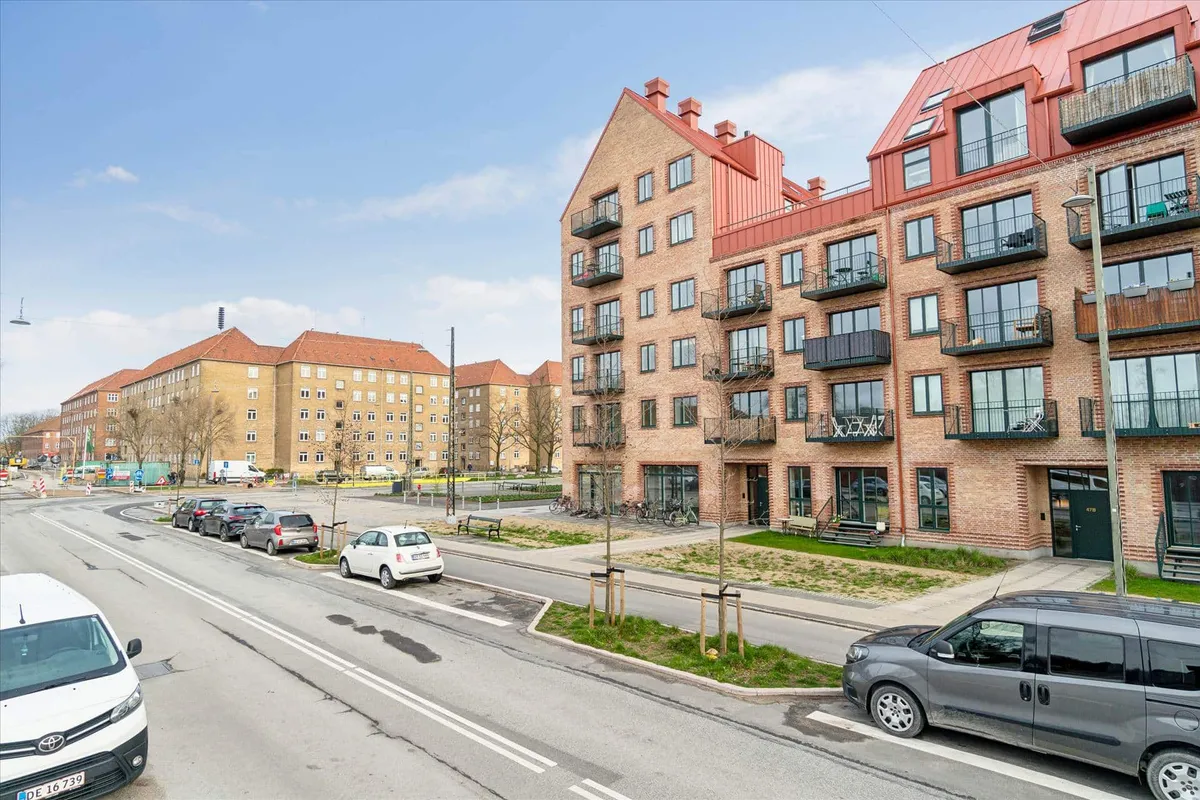 En stor hjørnebygning med mange lejligheder og et parkeringsområde med biler parkeret langs gaden