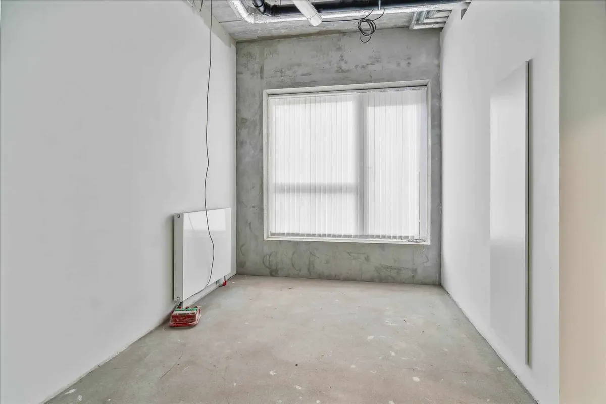 Tomt rum med hvid væg, vinduesruder, og hjørne med gulv, uden møbler og indretning.