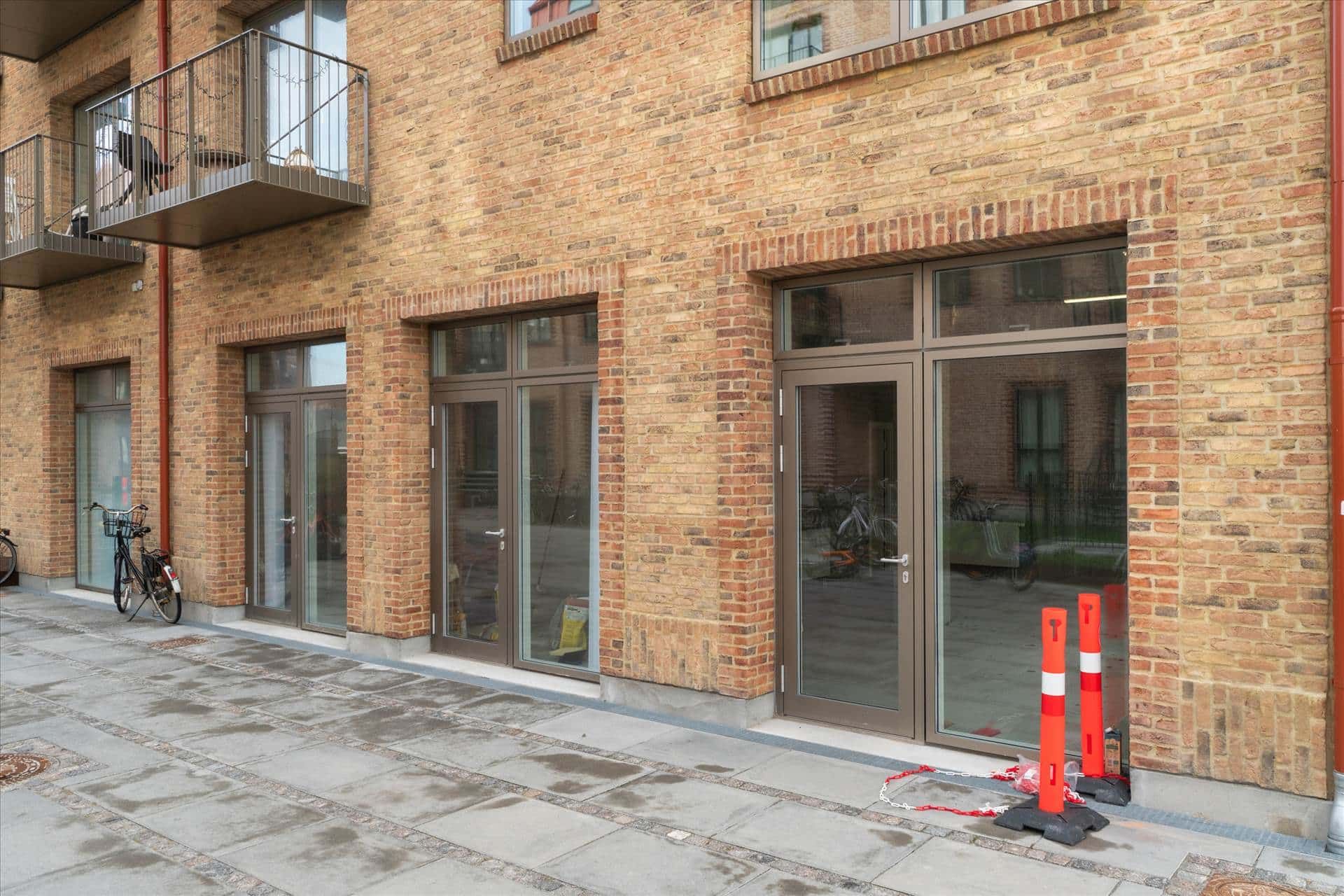 Moderne nyopført lejlighedsbygning med terrasse, glasdøre og vinduer, samt rødt gulv og to bjælkehinder på gaden