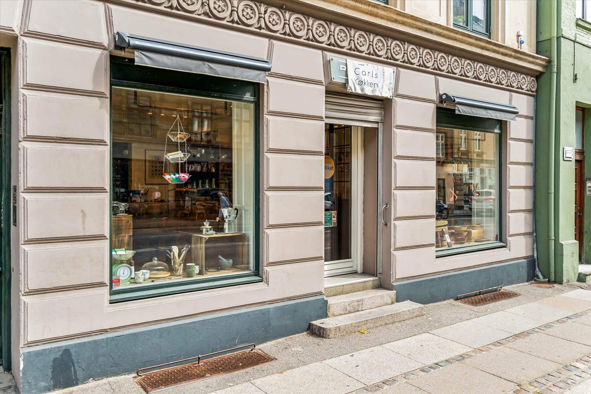 Butik med grøn facade og udskåret ornament, der hedder Carls Køkken med udsmykkede vinduer og trin foran døren