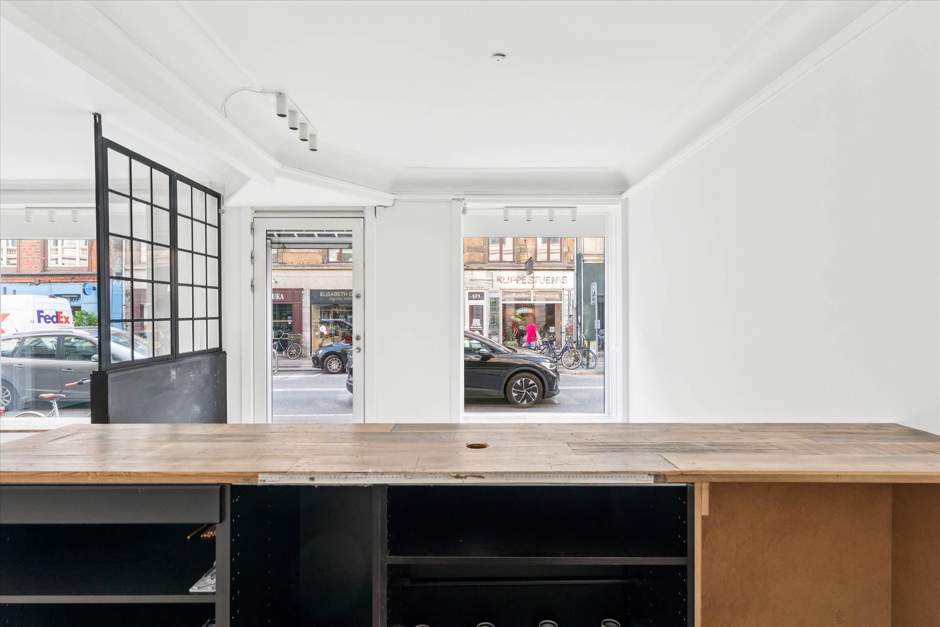 Solrigt kontorlokale med moderne møbler og glasdøre og vinduer med udsigt til en gade med biler og folk