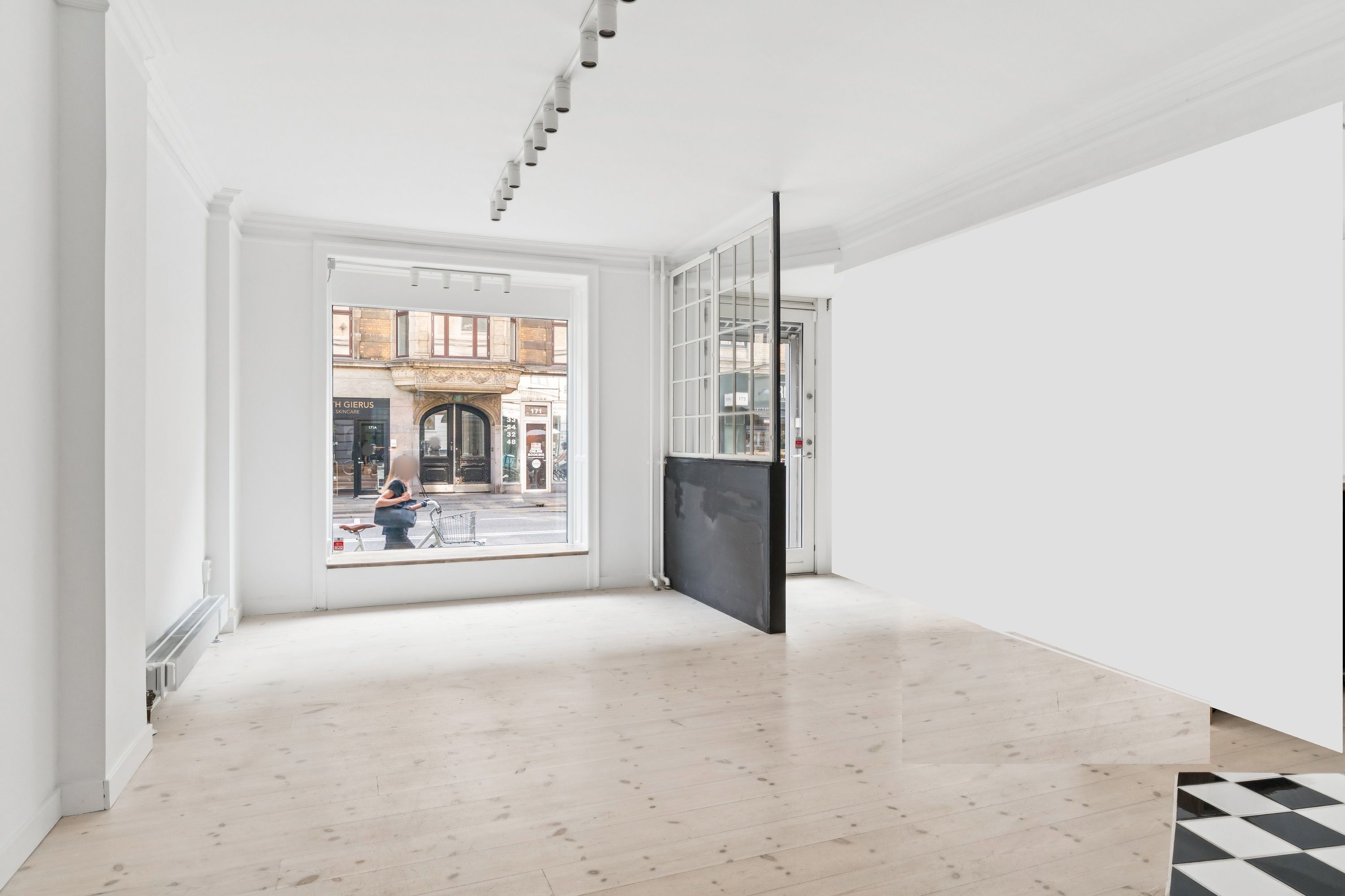 Et moderne, minimalistisk kontor med hvidt panel og lysegult gulv, åbne glasdøre og slanke lysekroner over hovedet, et svart metaldør på højre side