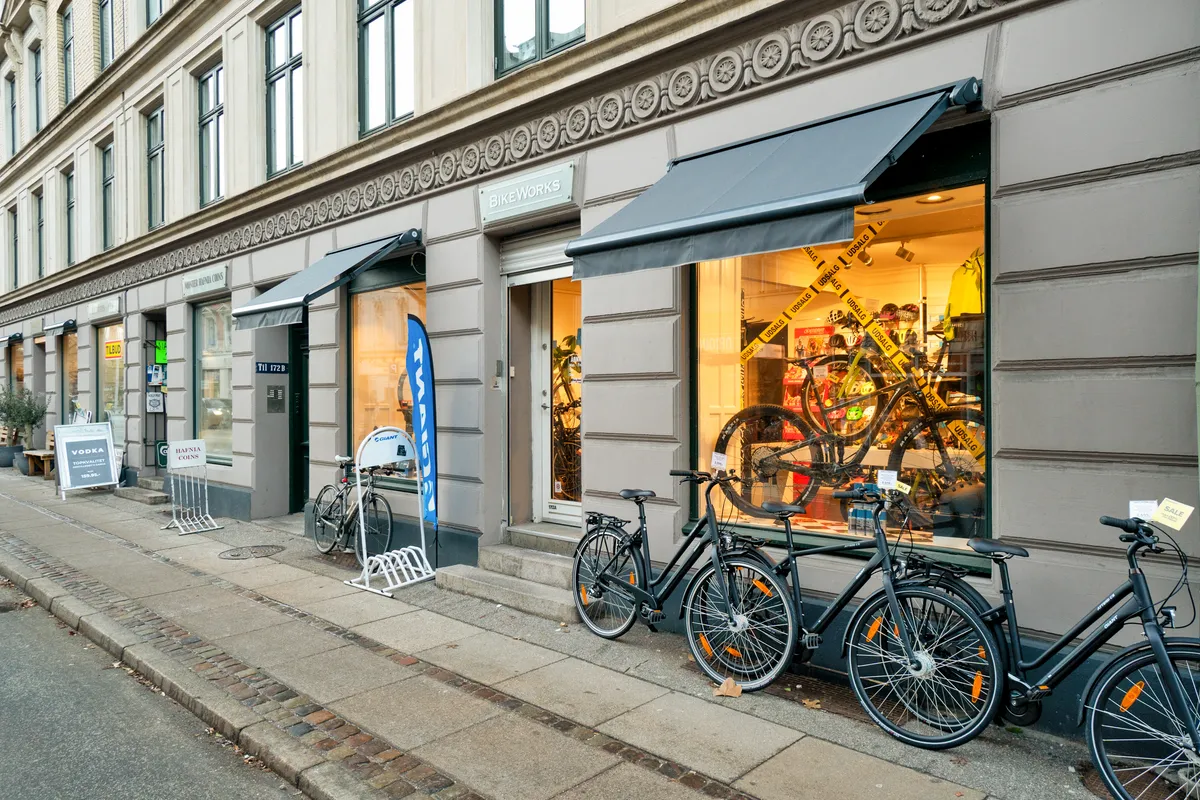 Butiksfront med udstillingsvindue og cykler udenfor, samt skilte med texten "BikeWorks" og tekst "Sale" på en gul etiketten