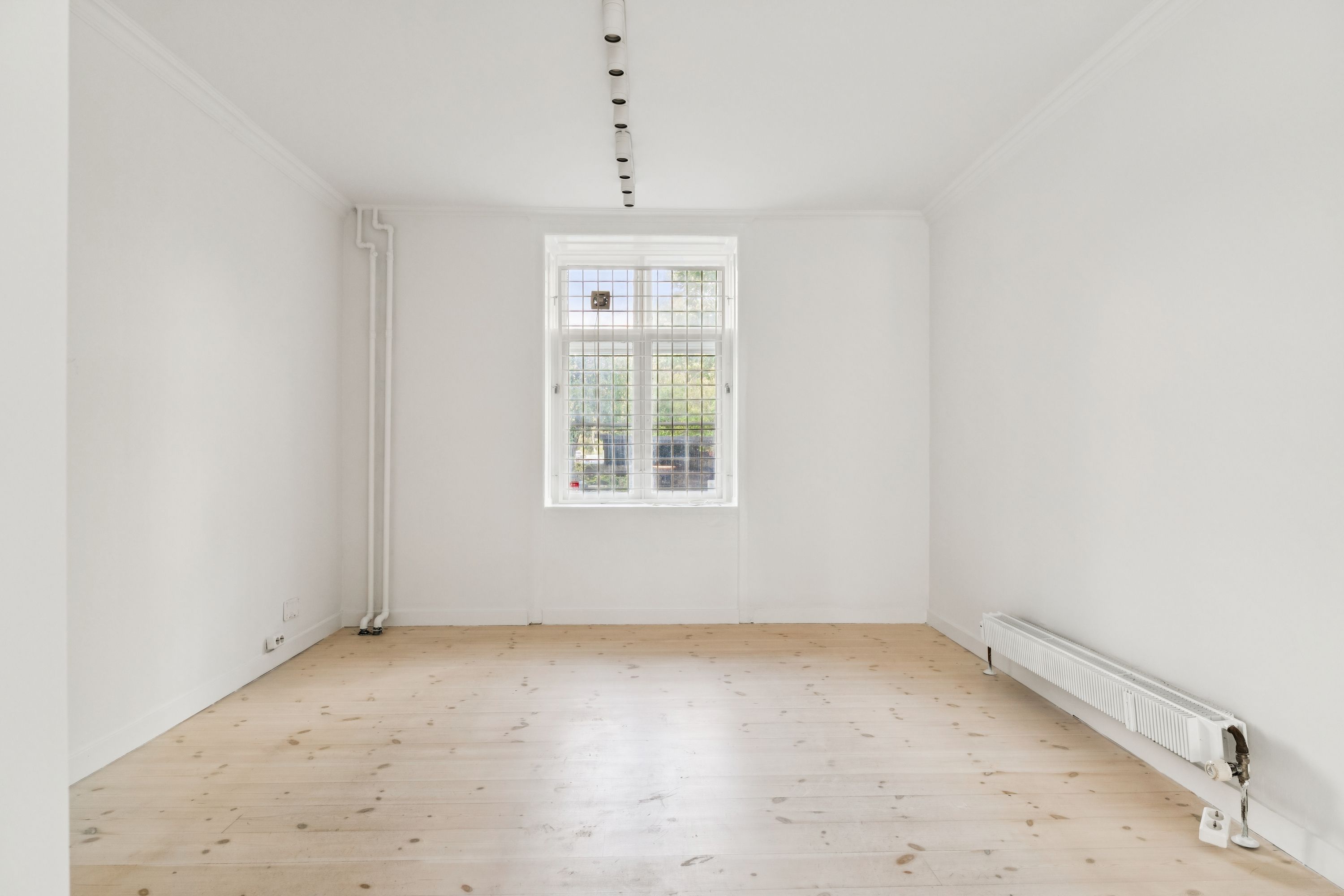 En tom hvid malet butikslokal med en stor glasdør og et hvidt radiator samt lysekroner på loftet