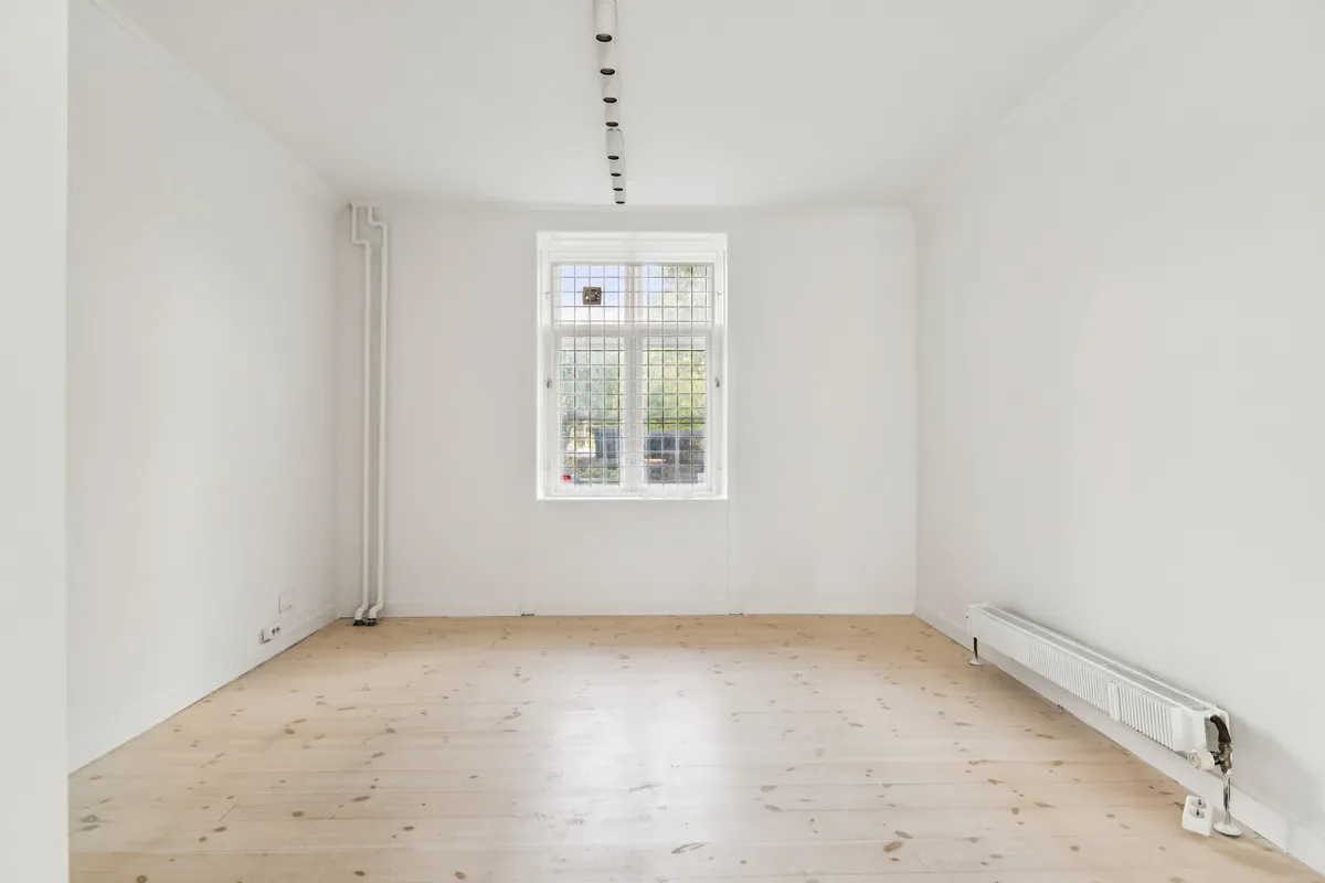 En tom hvid malet butikslokal med en stor glasdør og et hvidt radiator samt lysekroner på loftet