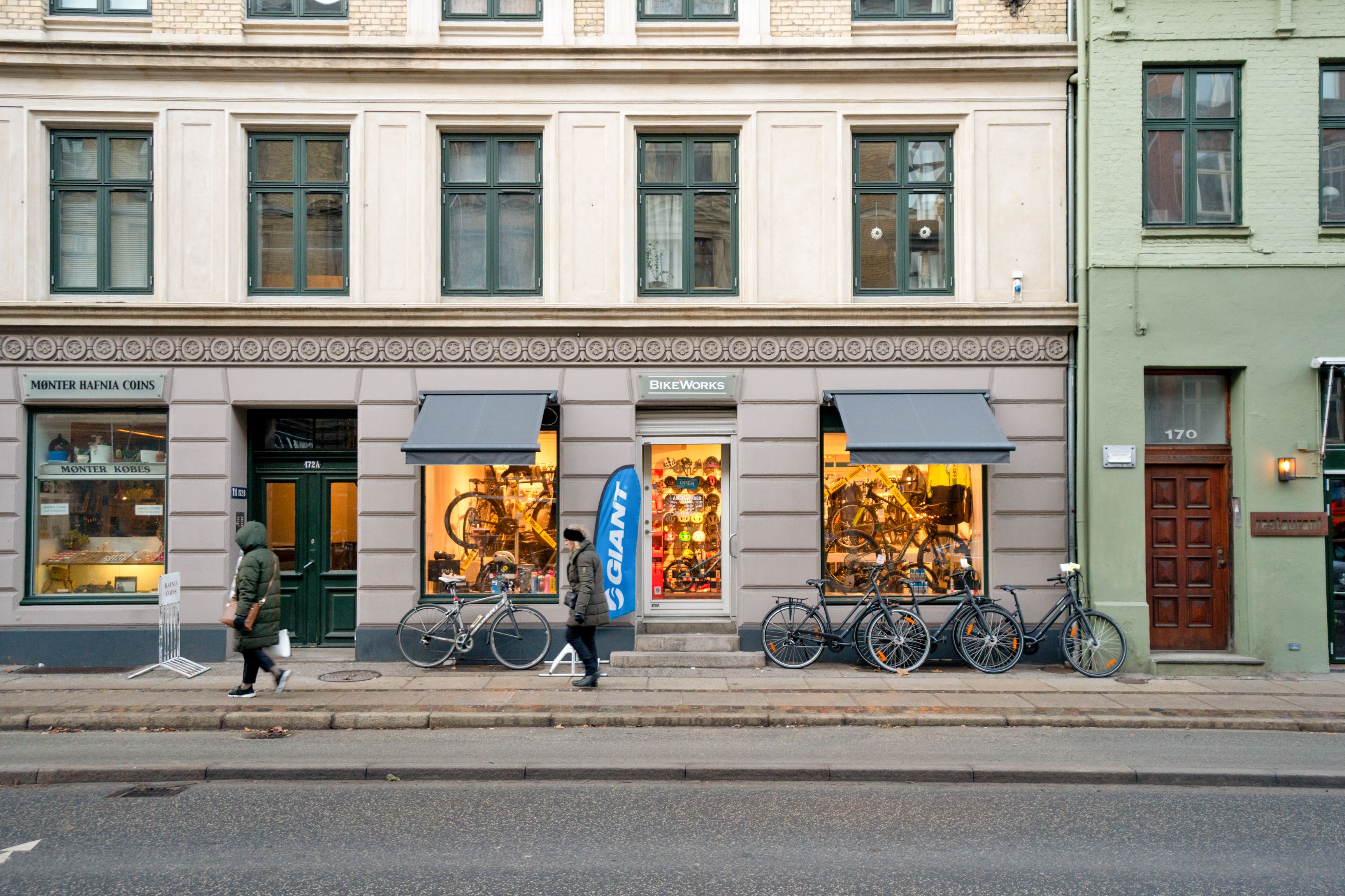To cykelhandlere går på gågaden foran Bikeworks og Monster Hafnia Coins-butikkerne på Gammel Kongevej i Frederiksberg. Tre cykler står udenfor Bikeworks-butikken.