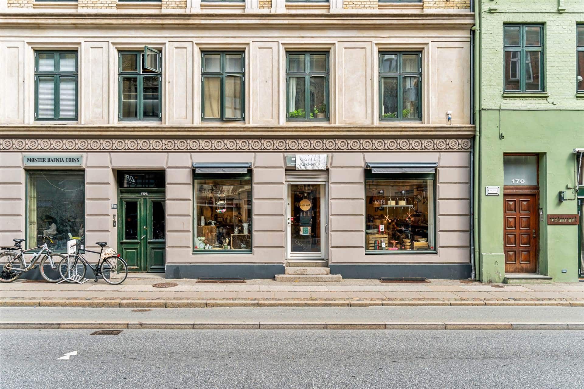 Butiksgade med grønne ruder og hængende cykler udenfor, facade med navnet Montér Hafnia Coins, lyserød facade med restaurant