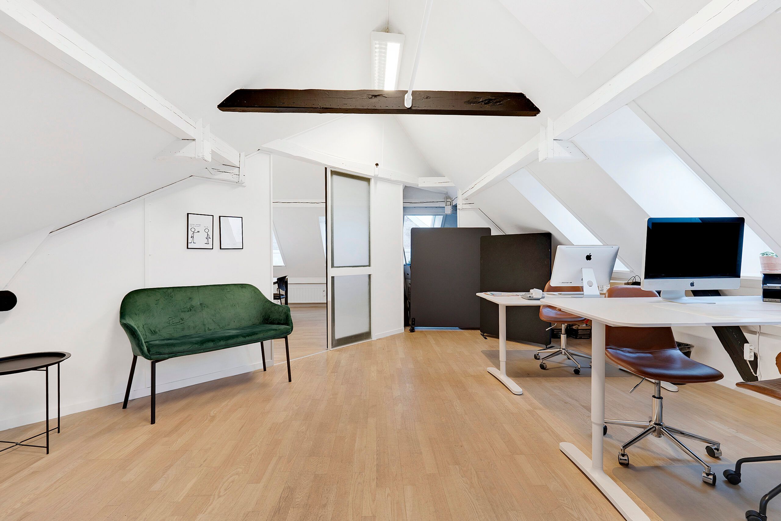 Kontor med lyse trægulve, højloft og højt vinduesglas, samt skriveborde og stole til at arbejde på