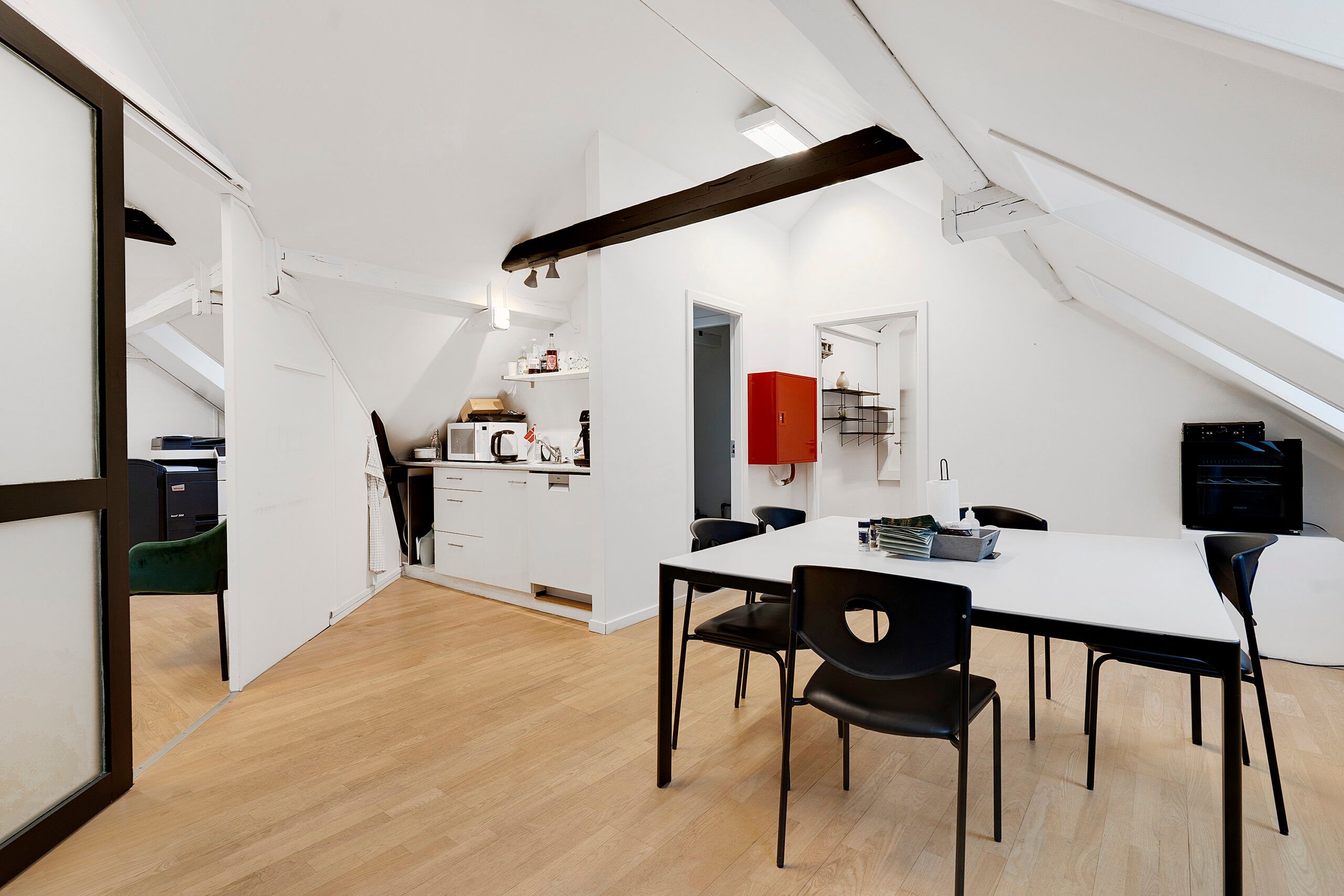 Loftsrum med højloft og moderne indretning med hvide vægge, lysegul trægulv og højt ophængt loftsbjælke. En moderne