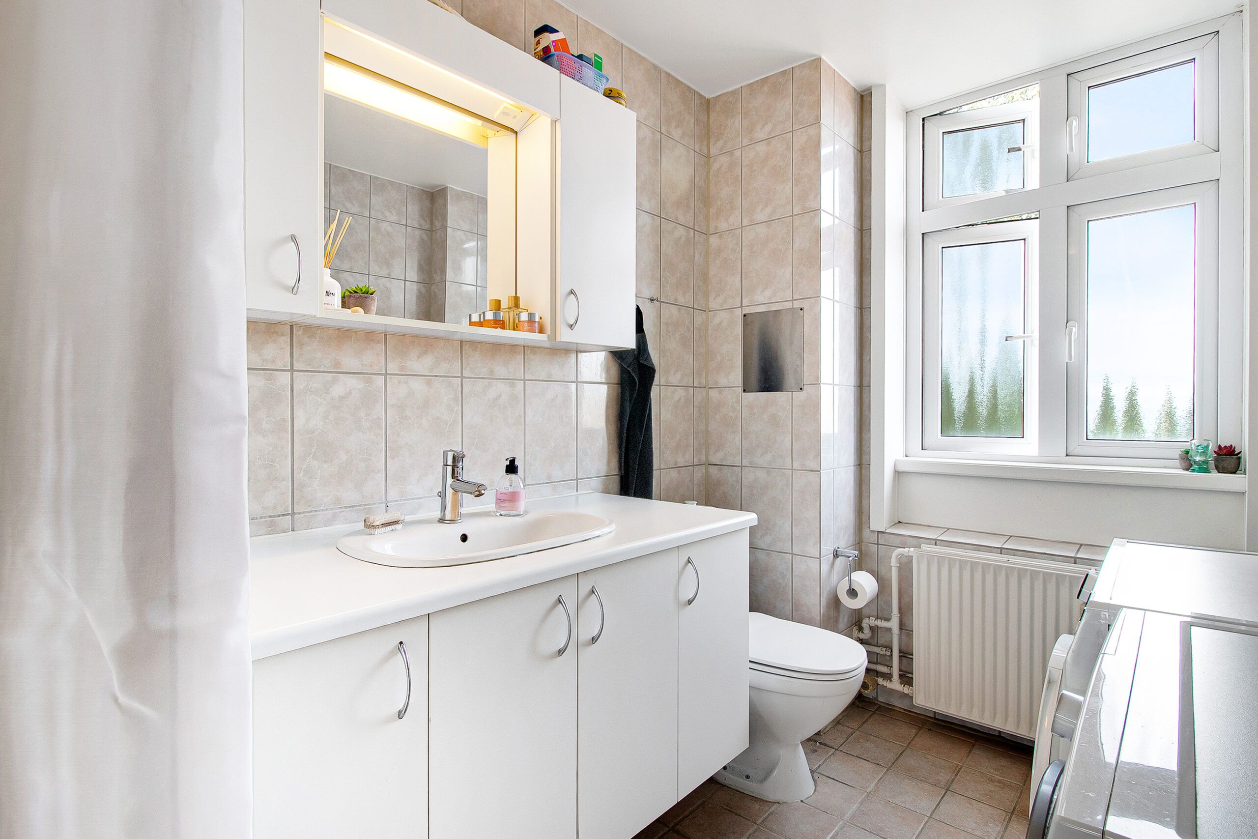 Et renligt badeværelse med hvide vægge og hængende toilet. Vaskebordet med lysegrå facader er udstyret med en hvid vask, et