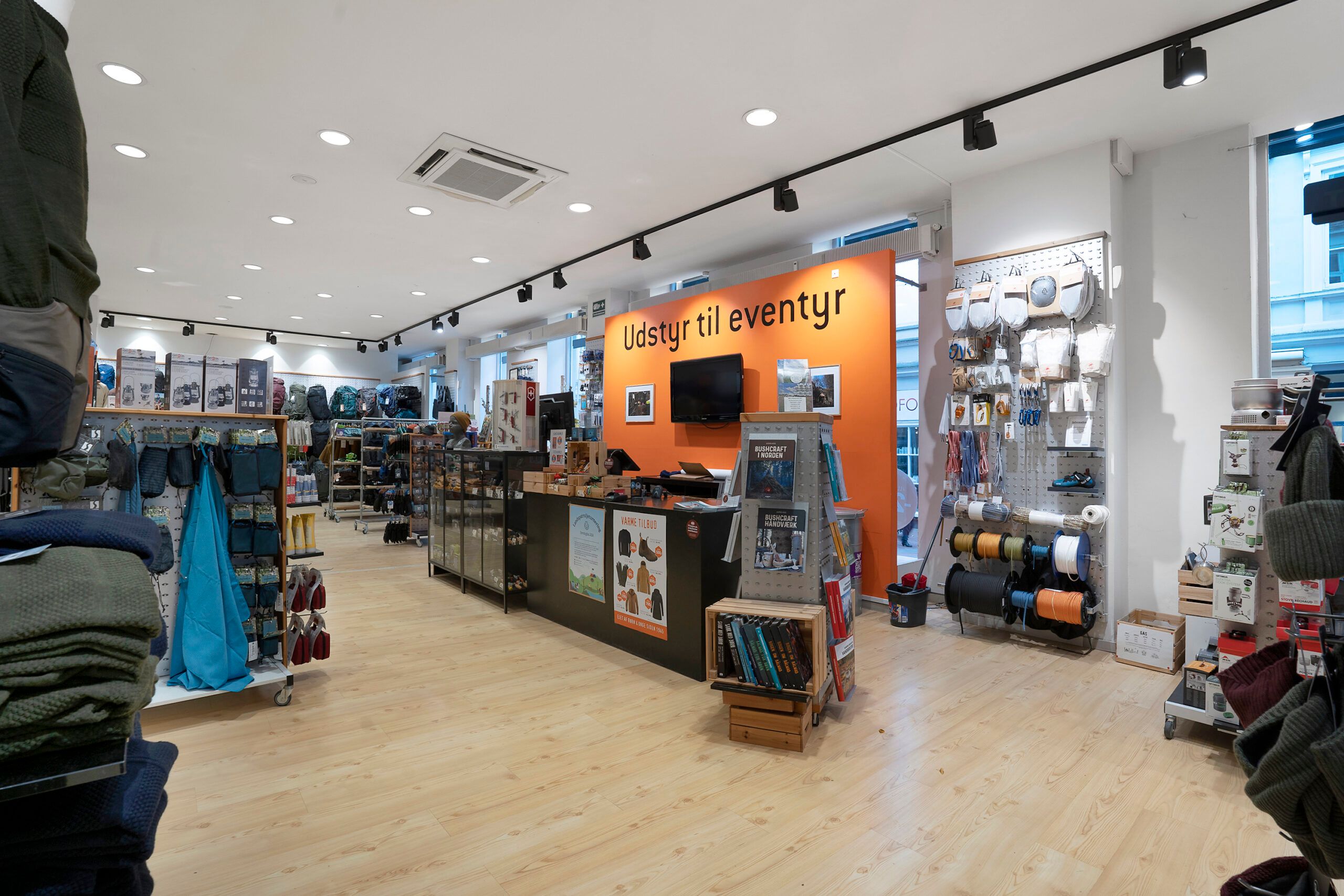 En indretning med campingudstyr, bukser og jakkestativer og tekst på væggen, der lyder Udstyr til eventyr