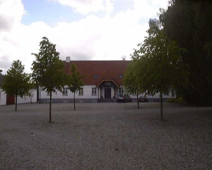 Store villaer med lyse facader og røde tag er omgivet af træer og stenoverdækning