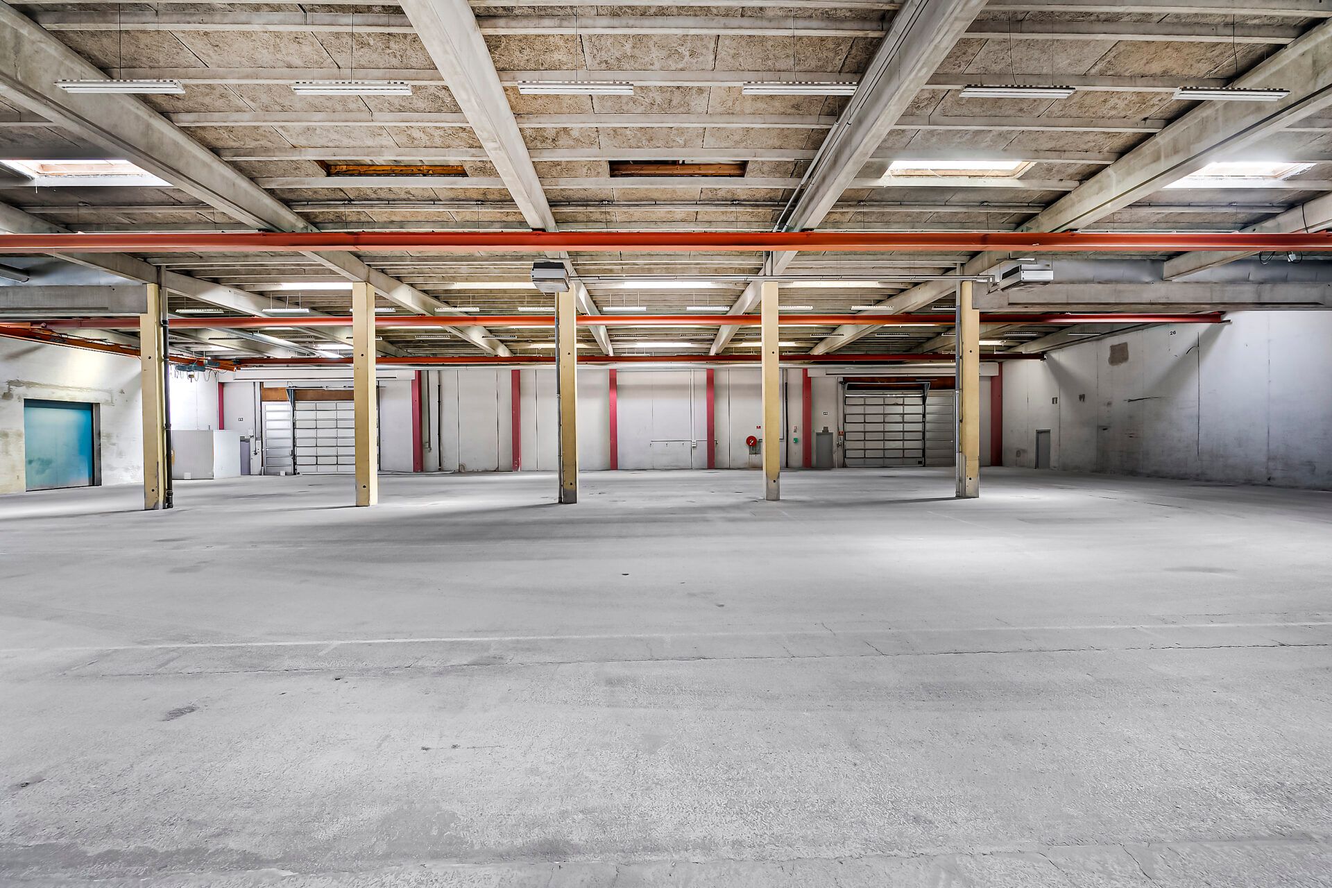 Lager med højt loft, gul gulv og røde bjælker. Højtloftede lager med røde bjælker og højtløbende lyskabler. Lager med røde