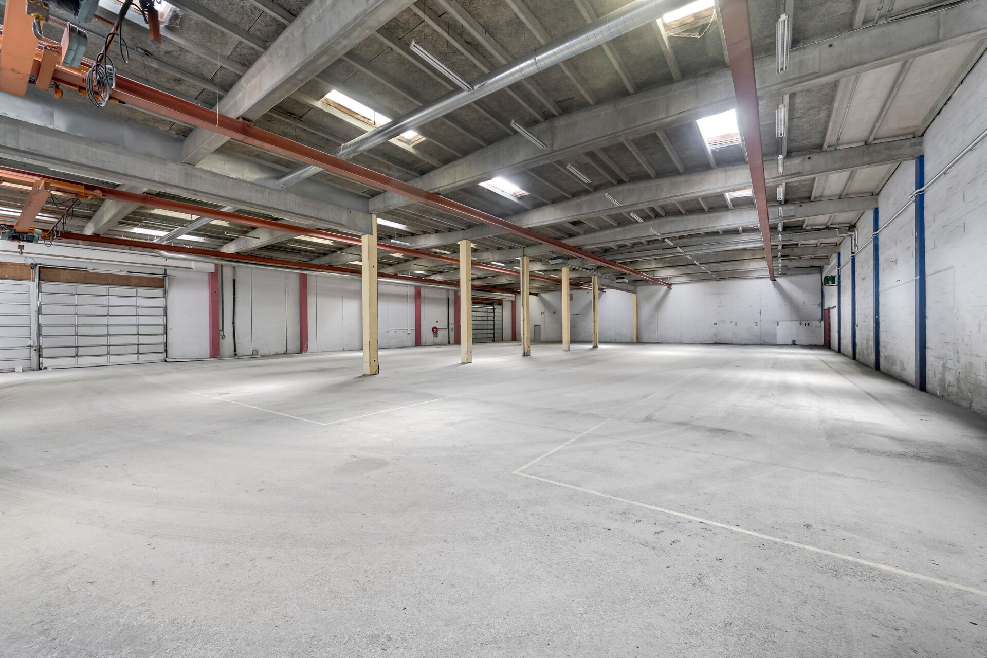 Lager med stort areal og 6 meters loftshøjde. Garagedør og lysekroner på loftet. Hjørnesøjler i midten af rummet