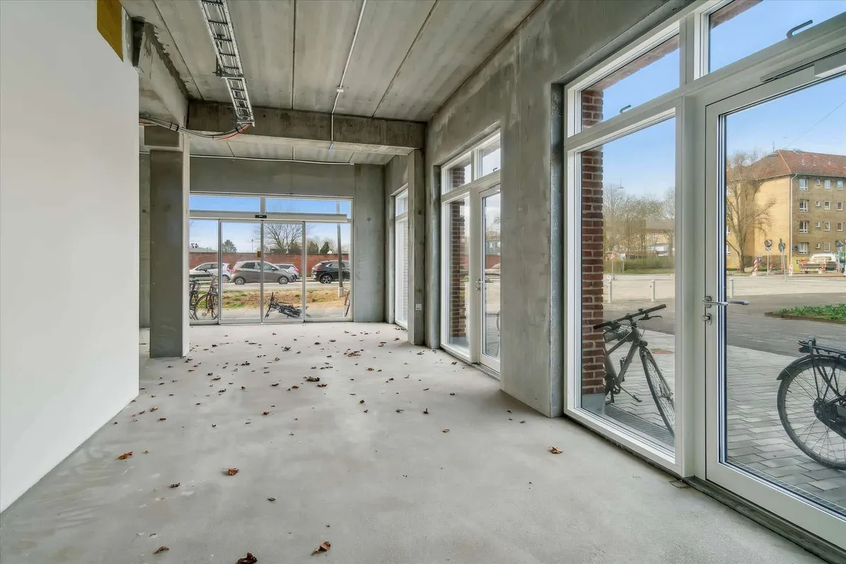 Værelse med store vinduer og glasdøre, der vender ud mod en parkeringsplads med to cykler og flere biler parkeret udenfor.