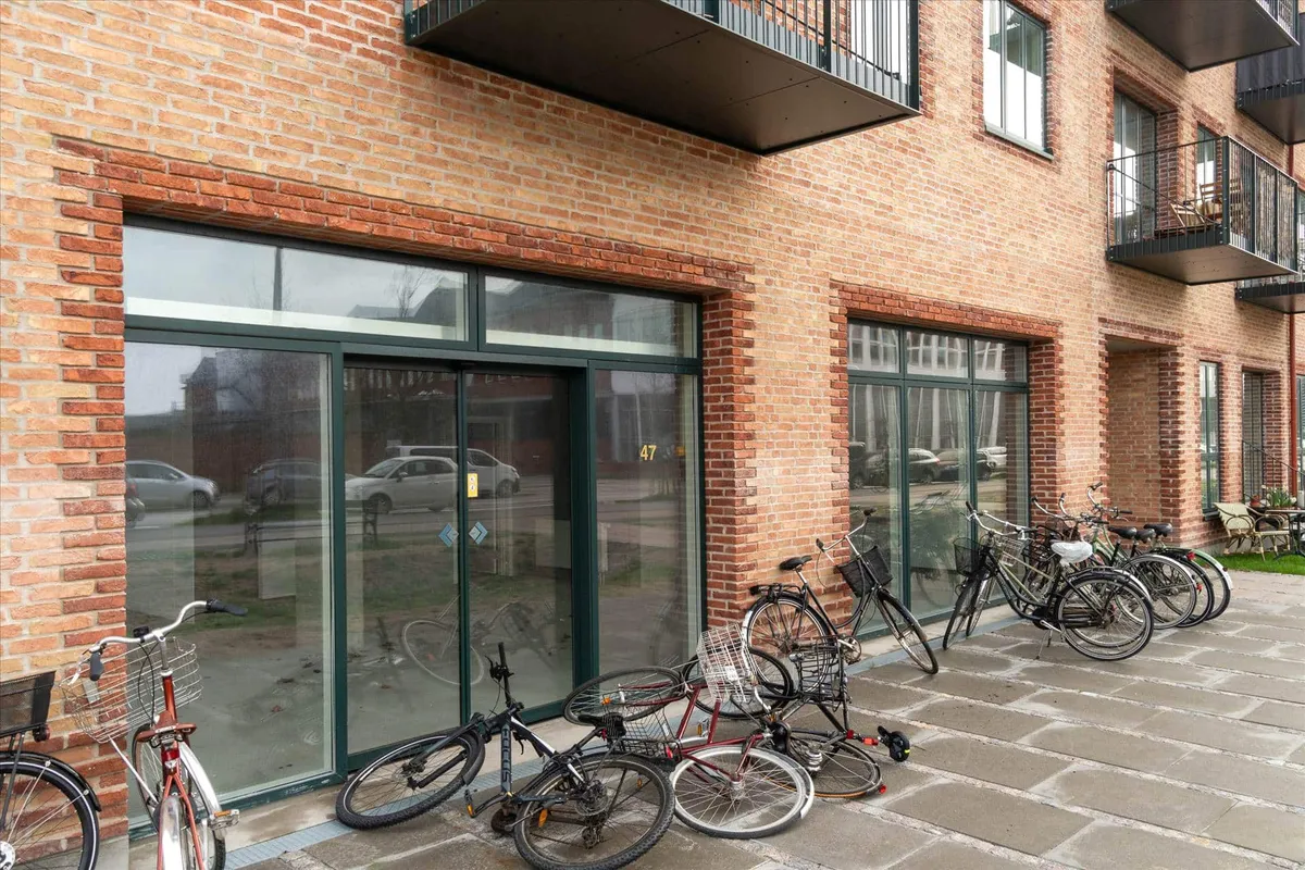 En række cykler er parkeret foran en bygning med store glasruder og terrasser med metalrækværk