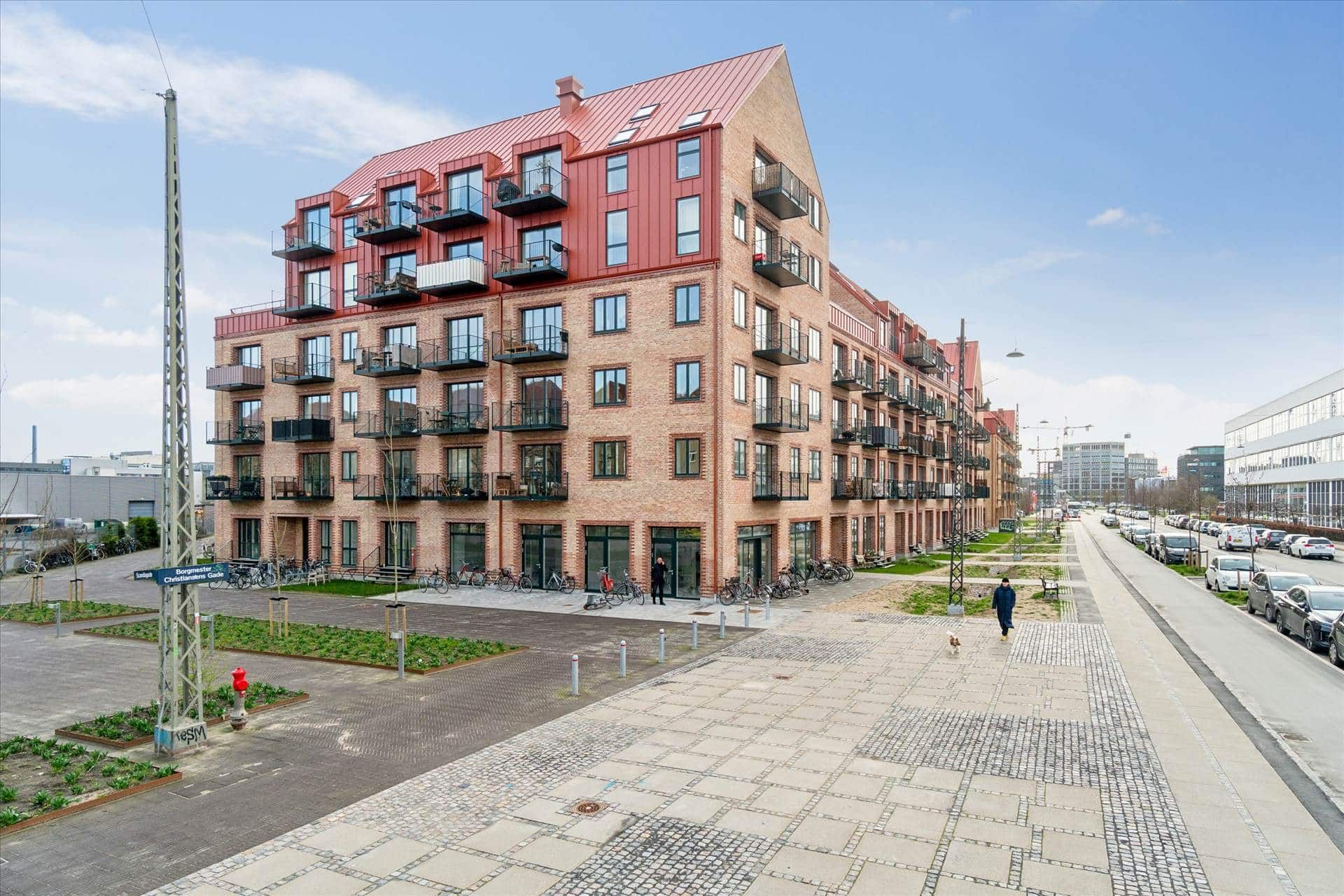 Nyopført lejlighedsbygning i Borgmester Christiansens Gade med balkoner, rødt tag og gårdhave med cykler og planter