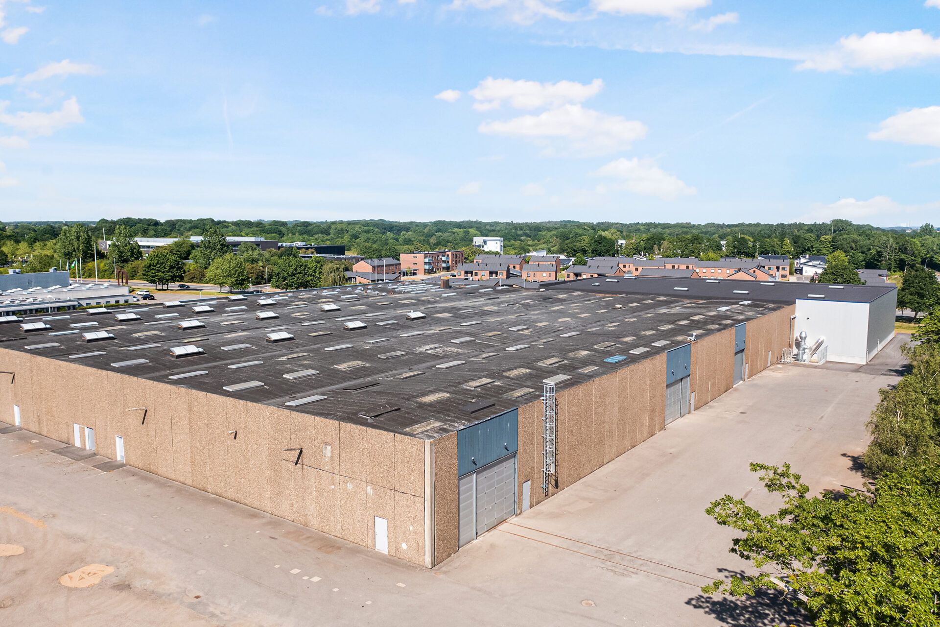 Yderst regulært lager med 6 meters loftshøjde, store garageporte og flere vinduer. Bygningen er omgivet af grønne træer og