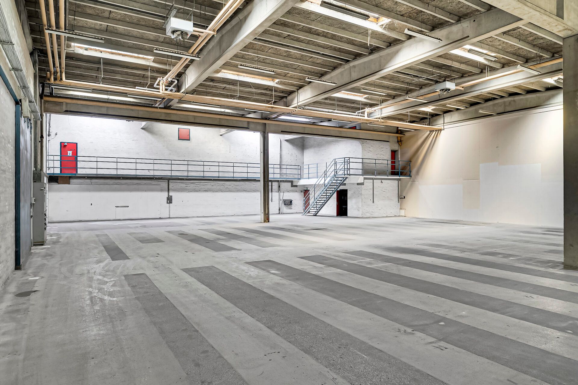 Lager med 6 meters loftshøjde og striber på gulvet og 2 rødlige døre samt en trappe i midten