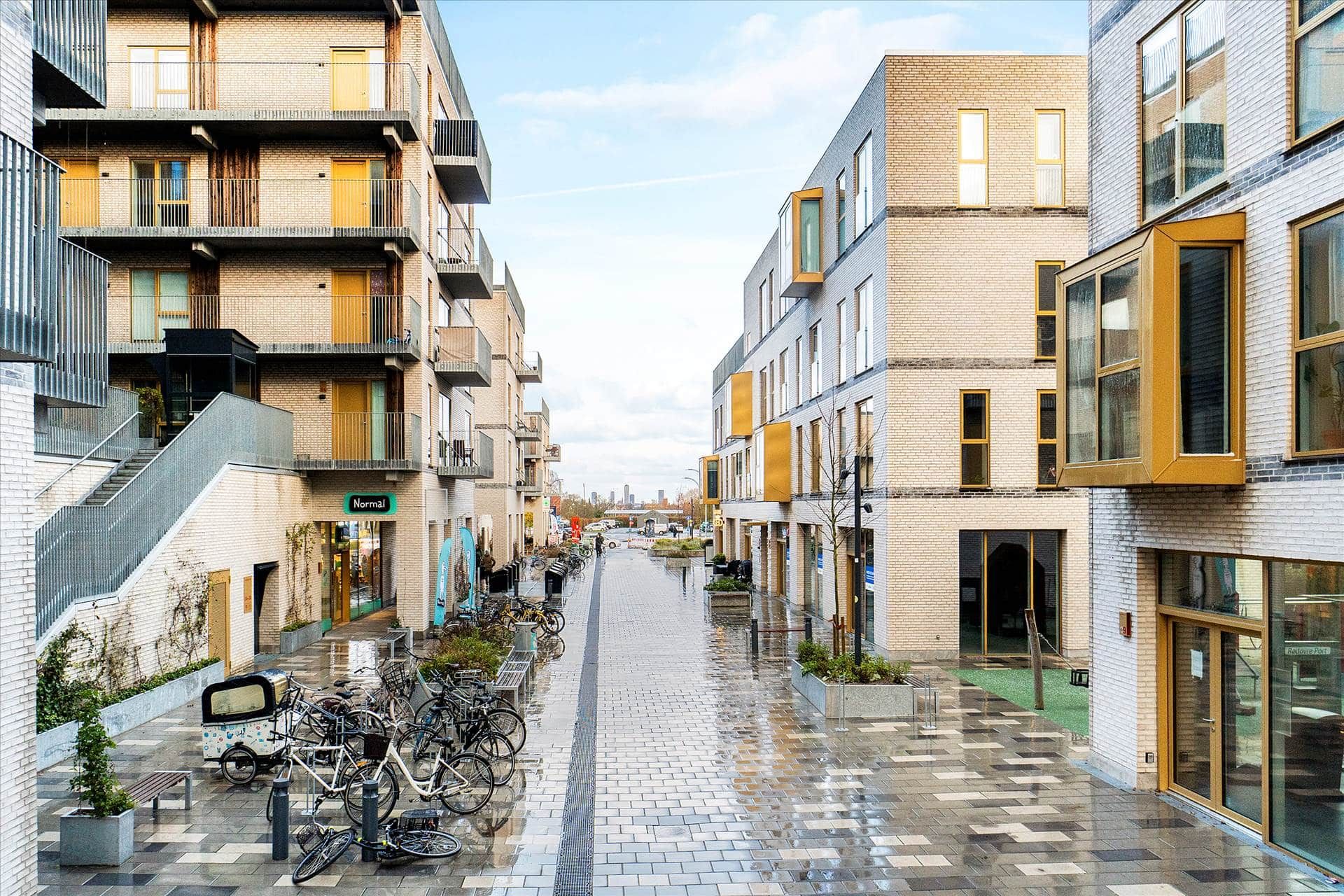 En række moderne bygninger med parkerede cykler og stier i Rødovre, hvor det er fugtigt efter regn