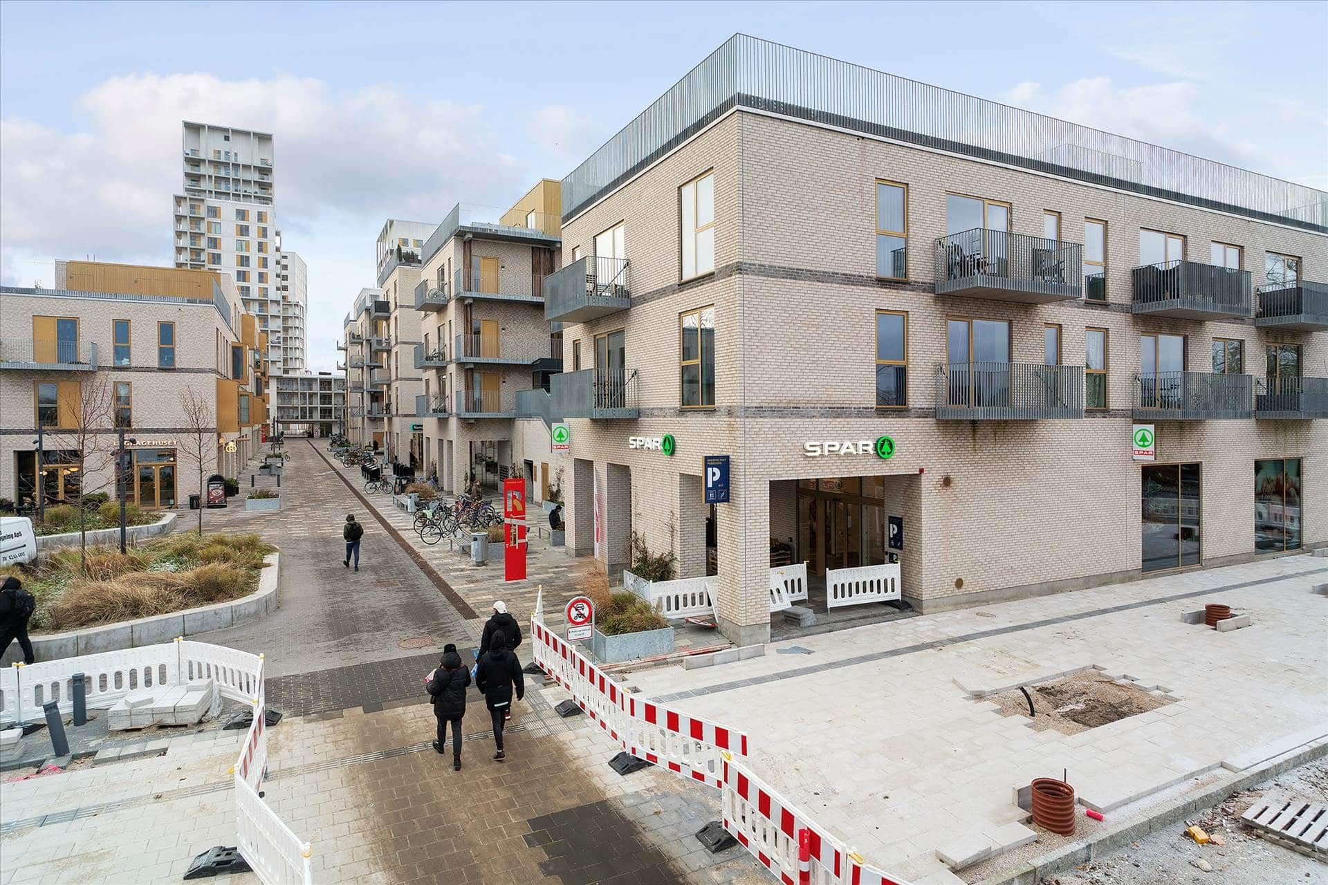 Mennesker går forbi butikker og bygninger på en gågade med en stor SPAR-butik og mærkede adgangsforbud