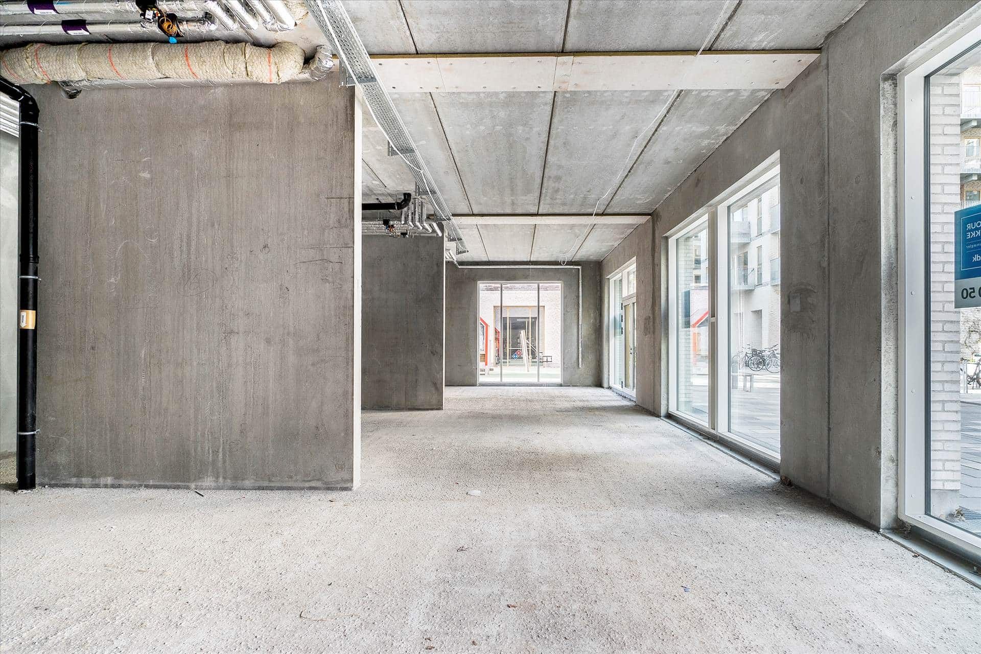 En stor, tom og nyrenoveret rum med høje, grå vægge og en glat, hvid gulv samt store glasruder og metalbælter i loftet