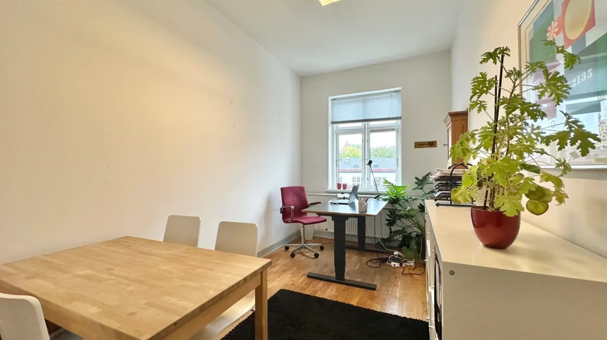 Lejlighed med to separate værelser og et køkken. Et skrivebord med en bærbar computer og et rødt stol står i det ene værelser