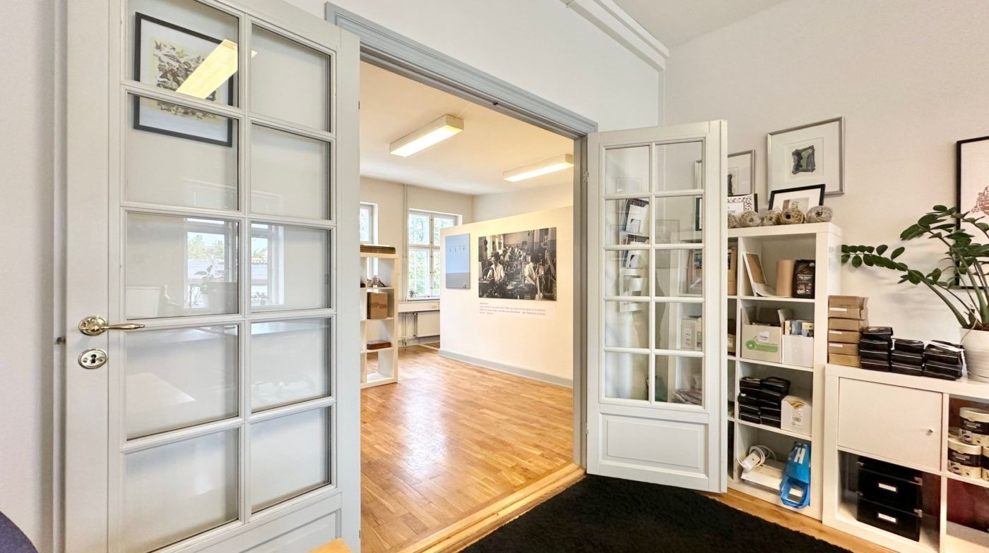 Hvidt rum med åbne døre og lyse gulve, højt loft med indbygget belysning, kunstværker og hylder med genstande og planter i