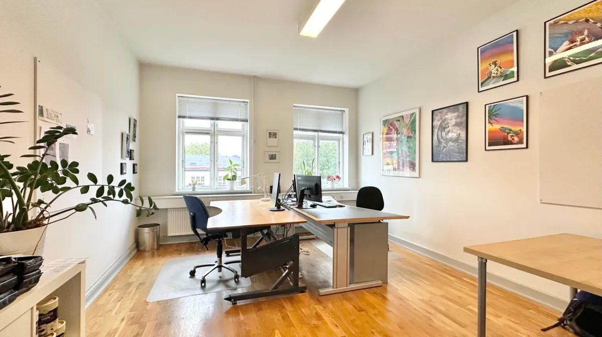 Kontor med to skriveborde og skrivebordsstole, skrivebordslamper, en plante og malerier på væggen