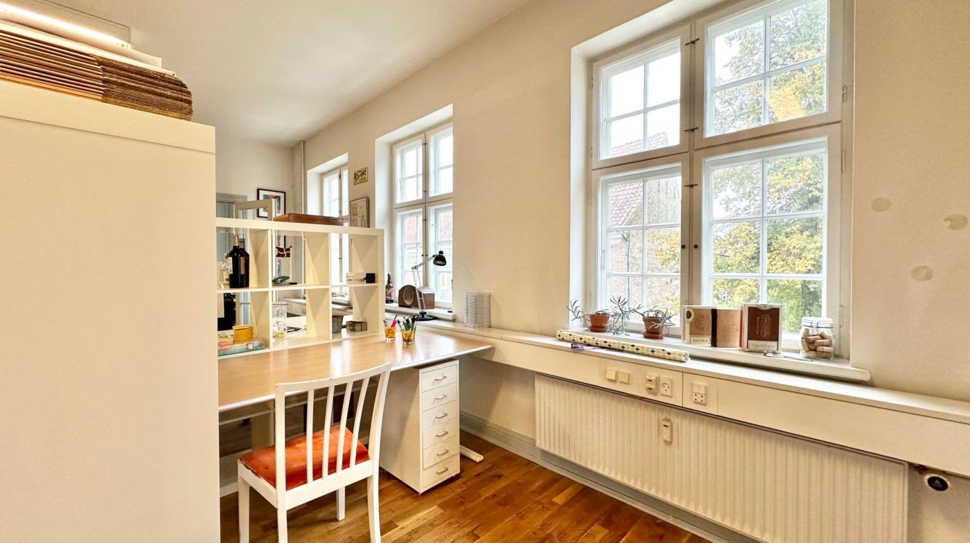 En hvid indretning med skrivebord, høj garderobe og en hvid lampe samt et radiatorpanel i gulvet