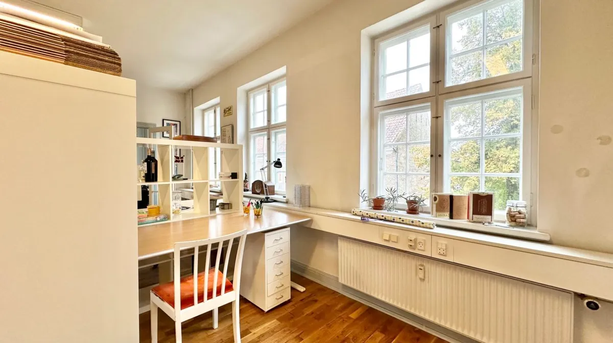 En hvid indretning med skrivebord, høj garderobe og en hvid lampe samt et radiatorpanel i gulvet