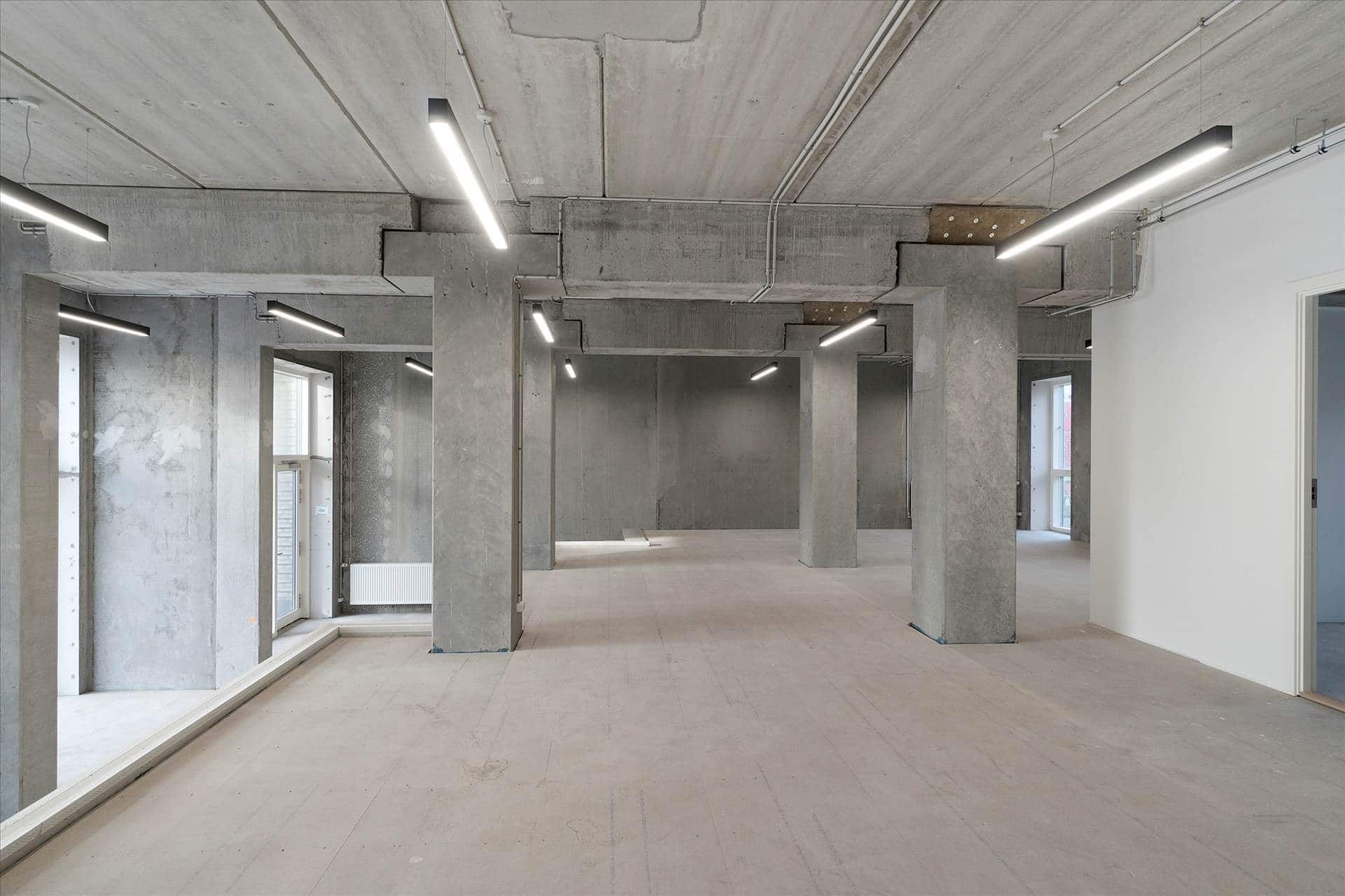 En stor og hvid stue med lyse gulve og lysegrå vægge og søjler samt åbne vinduer og døre