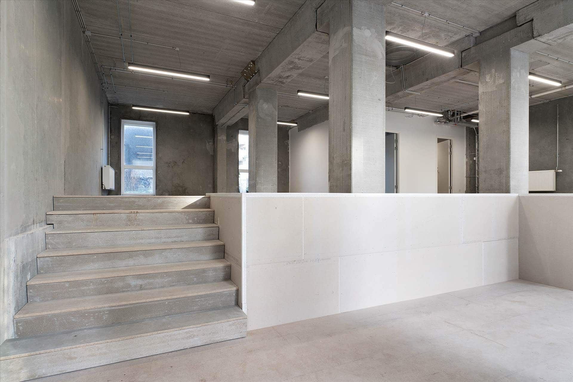 En stor åben rum med flere trin, høje hvide vægge og cementgulve samt indbyggede lysekroner