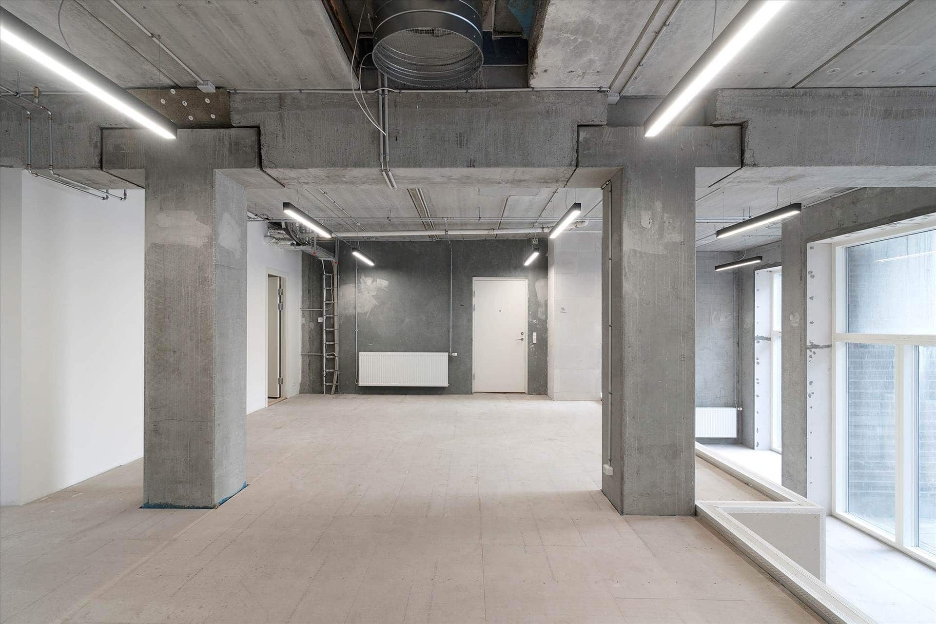 En stor, tom erhvervslokal med højloft, hvidt gulv og store vinduer med store hvide rammer