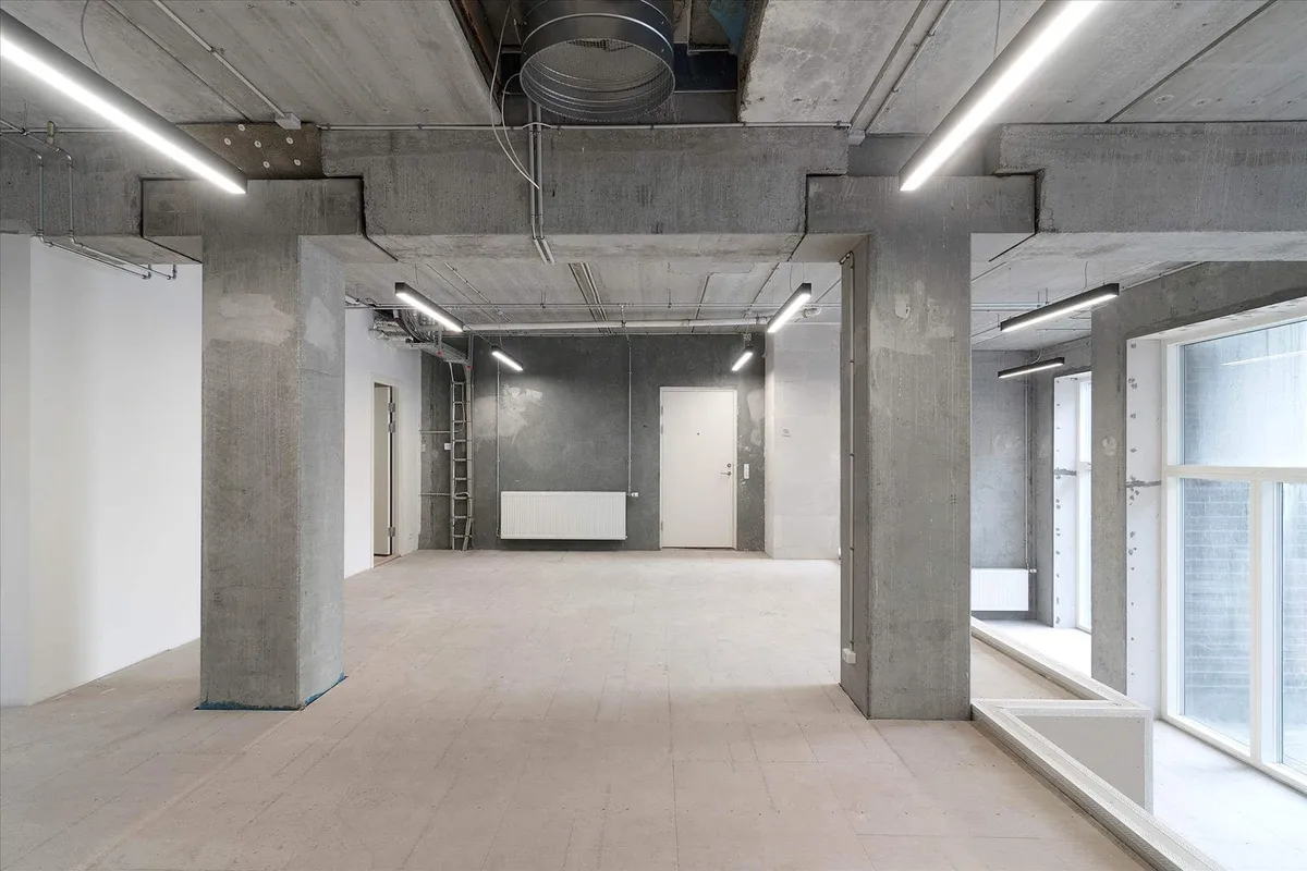 En stor, tom erhvervslokal med højloft, hvidt gulv og store vinduer med store hvide rammer